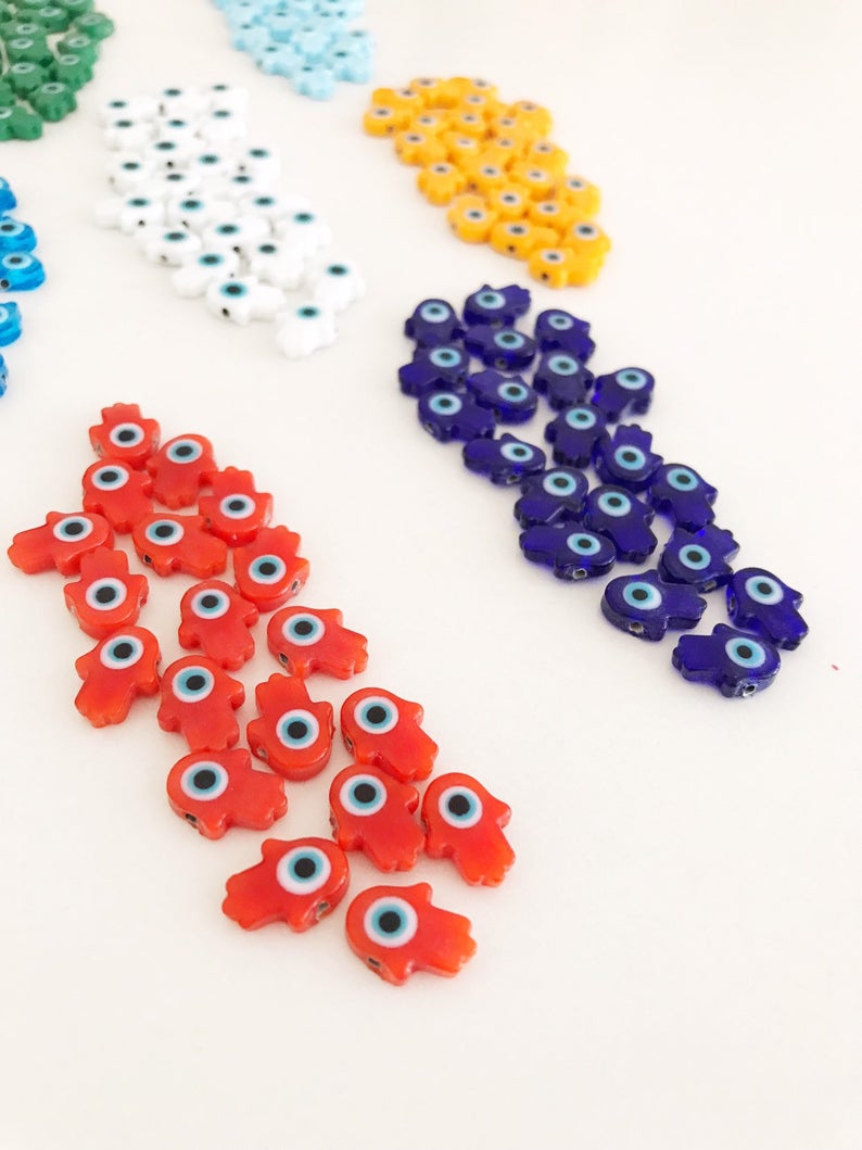 A collection of 10 handmade glass hamsa evil eye spacer beads in various colors, showcasing their intricate designs and craftsmanship.