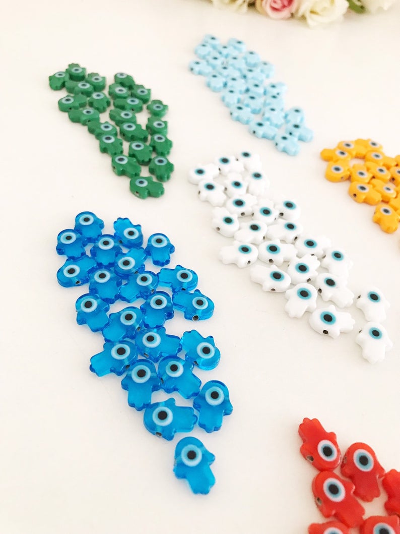 A collection of 10 handmade glass hamsa evil eye spacer beads in various colors, showcasing their intricate designs and craftsmanship.