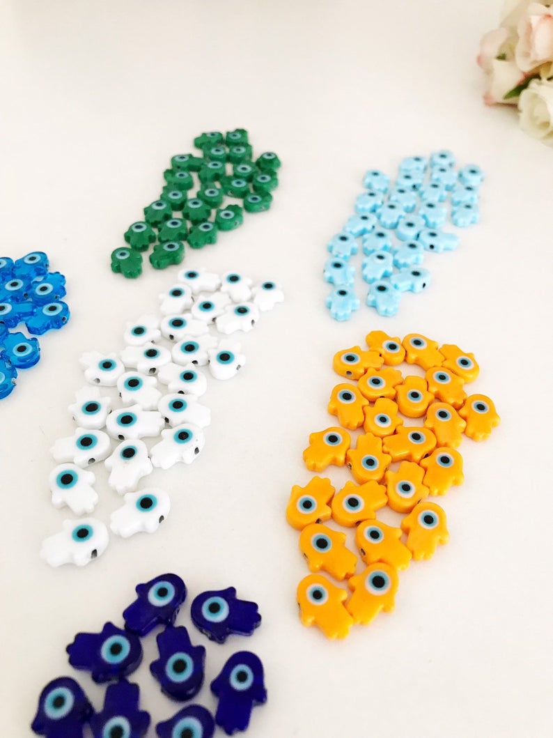 A collection of 10 handmade glass hamsa evil eye spacer beads in various colors, showcasing their intricate designs and craftsmanship.