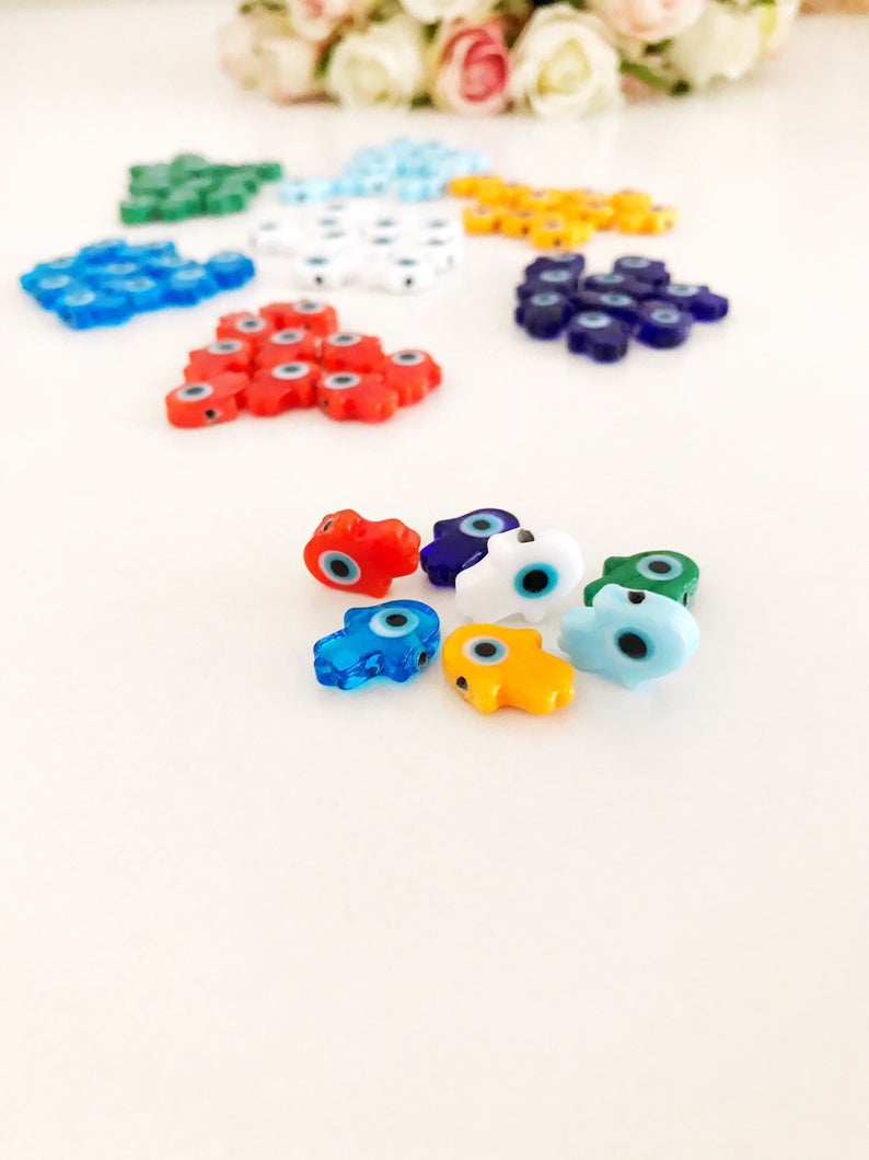 A collection of 10 handmade glass hamsa evil eye spacer beads in various colors, showcasing their intricate designs and craftsmanship.