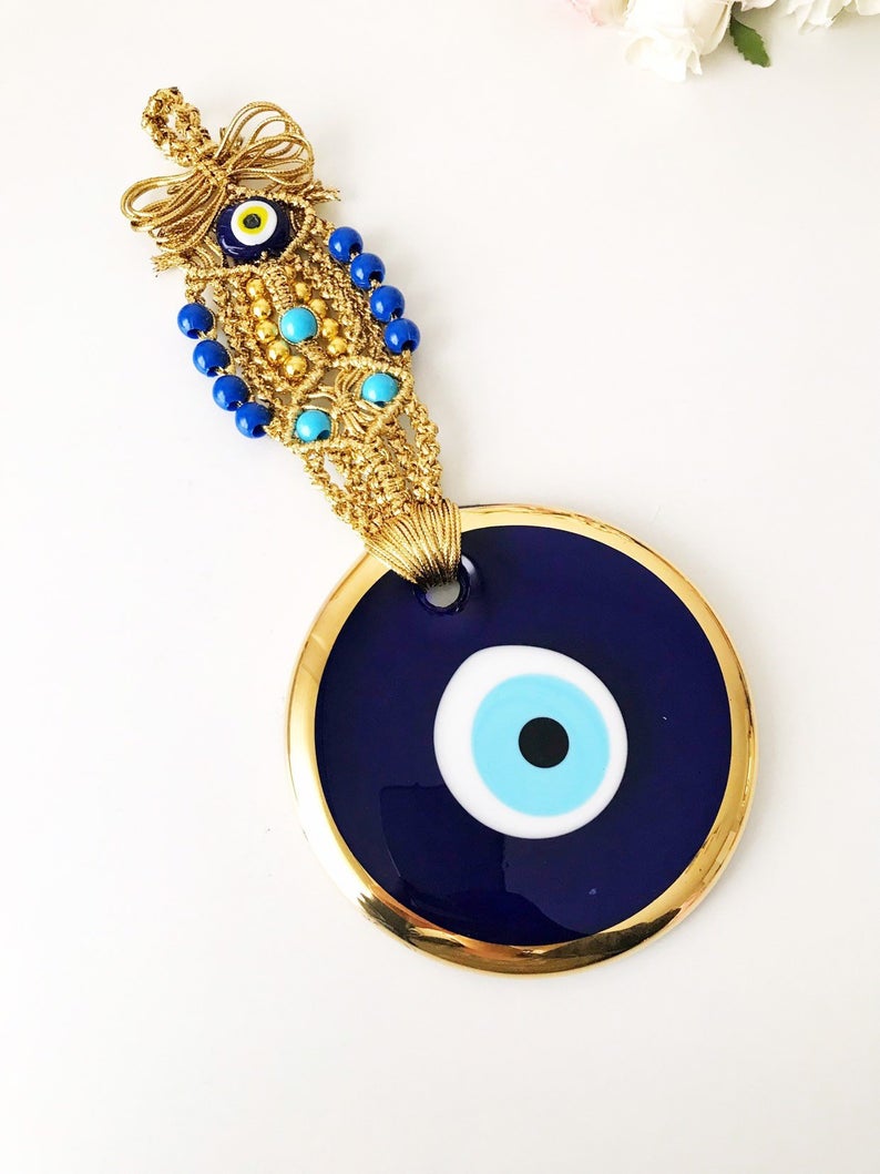 A beautiful gold evil eye wall hanging featuring blue evil eye beads and intricate macrame design, symbolizing protection and good luck.