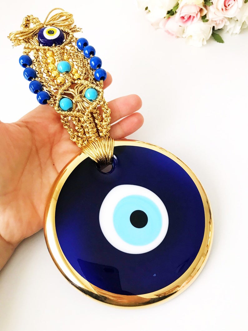 A beautiful gold evil eye wall hanging featuring blue evil eye beads and intricate macrame design, symbolizing protection and good luck.