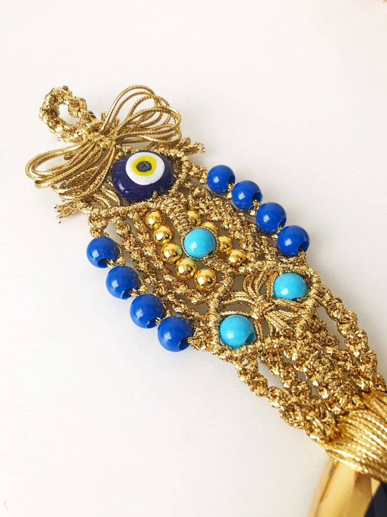 A beautiful gold evil eye wall hanging featuring blue evil eye beads and intricate macrame design, symbolizing protection and good luck.