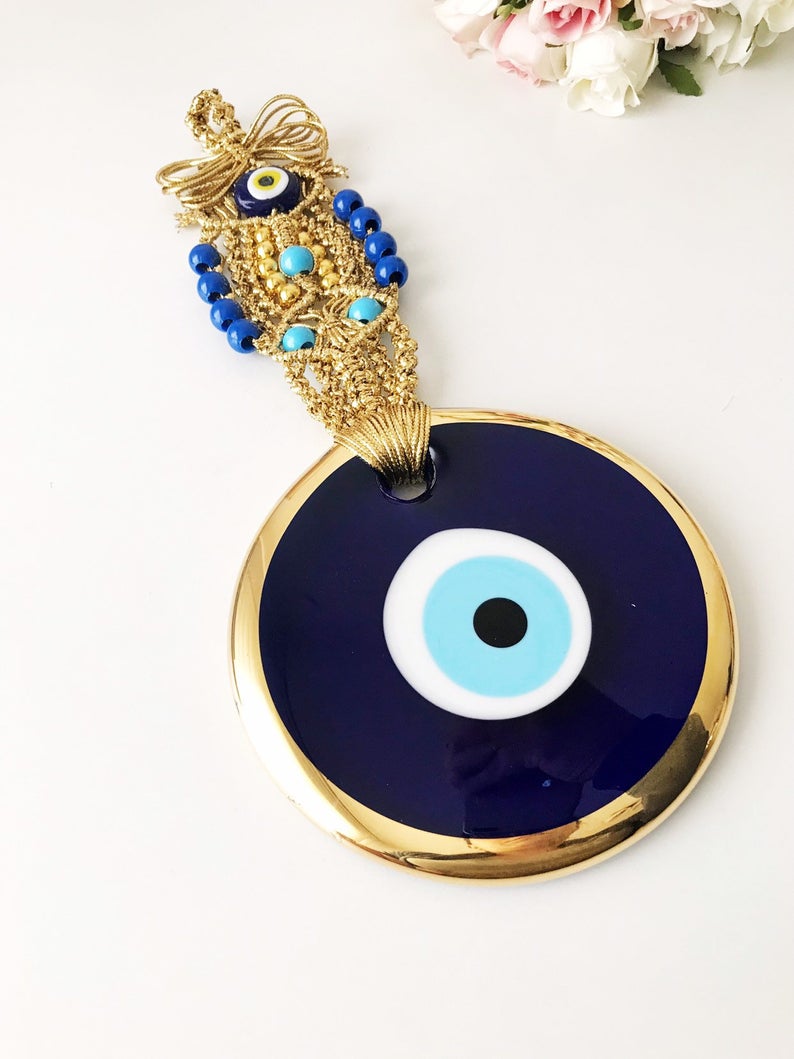 A beautiful gold evil eye wall hanging featuring blue evil eye beads and intricate macrame design, symbolizing protection and good luck.