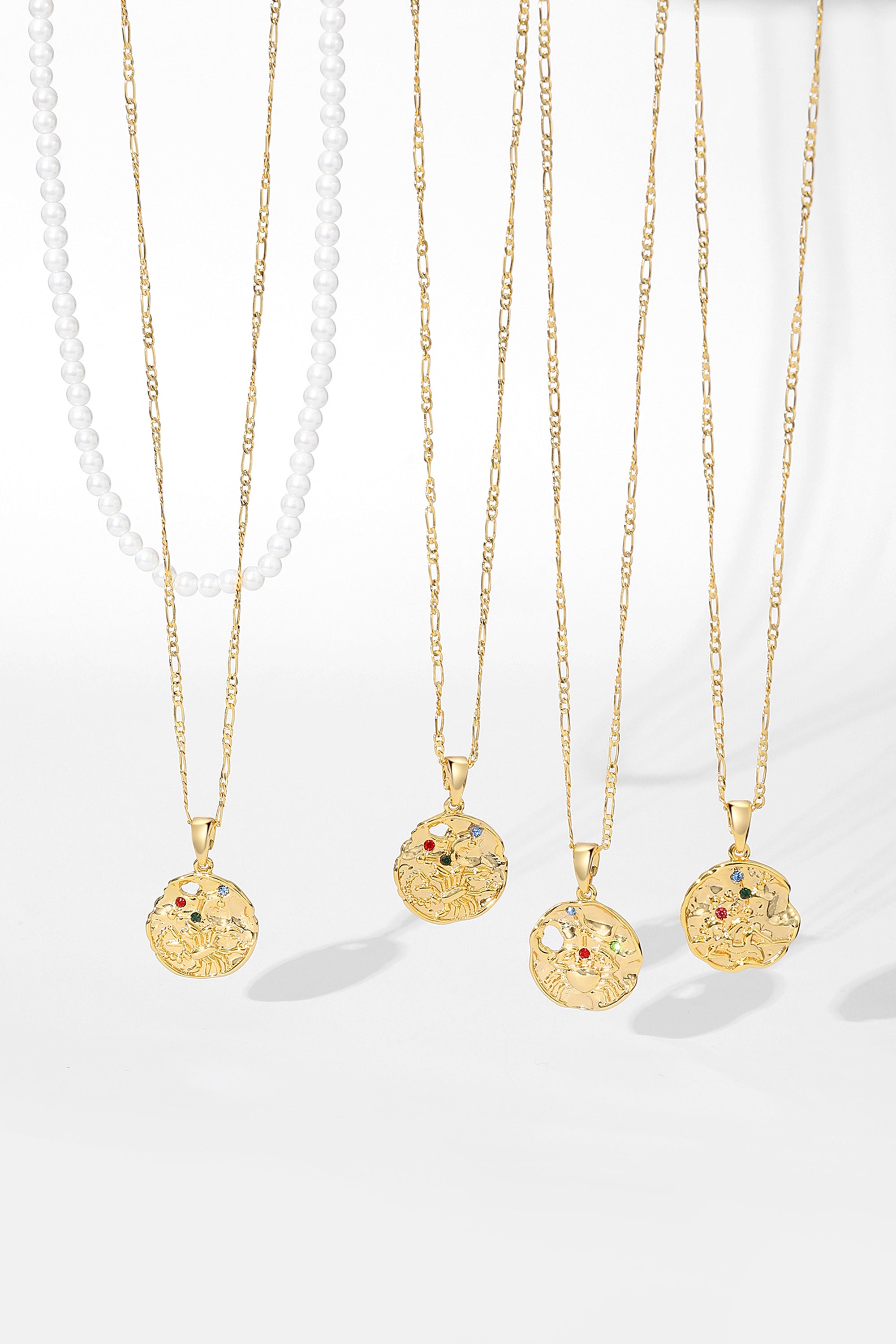 Gold Sculptural Zodiac Sign Pendant Necklace Set featuring an engraved zodiac charm, pearl necklace, and gold figaro chain.