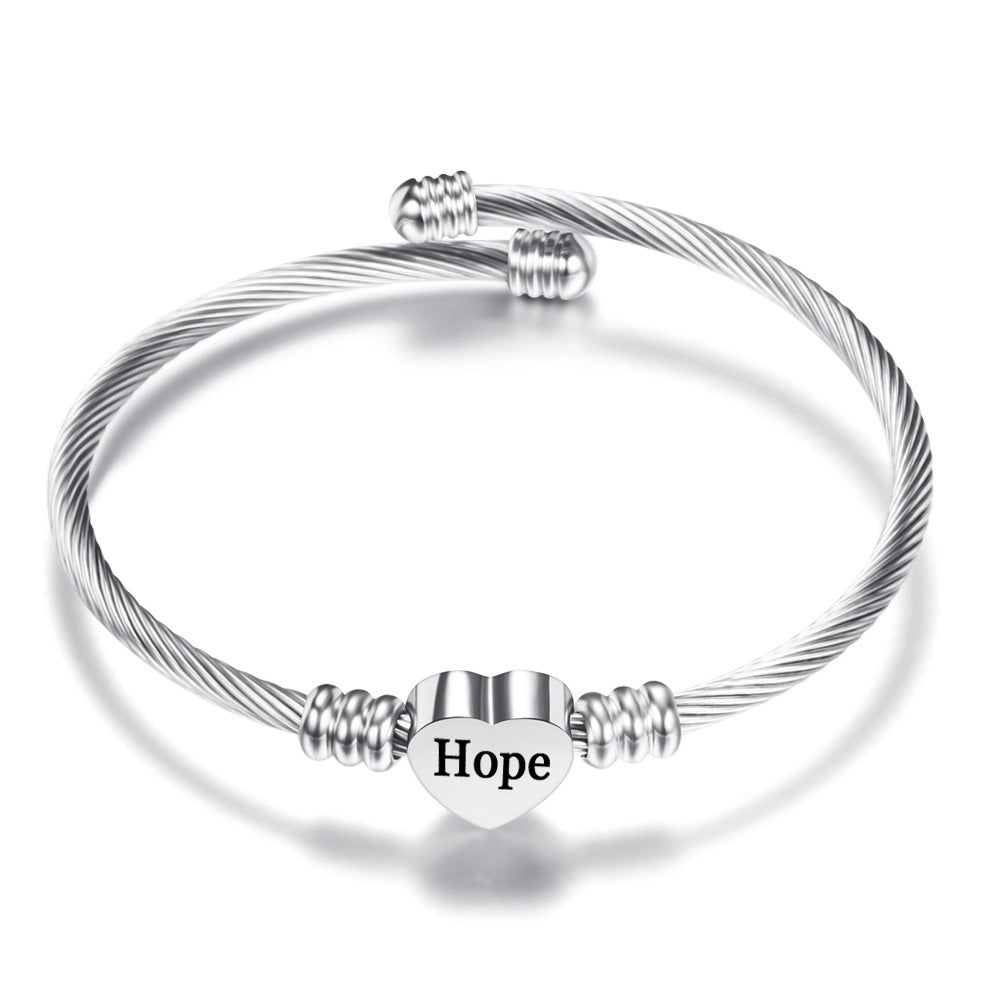 A high-polished stainless steel charm bangle featuring a heart initial charm and a heart quote charm, symbolizing hope and love.