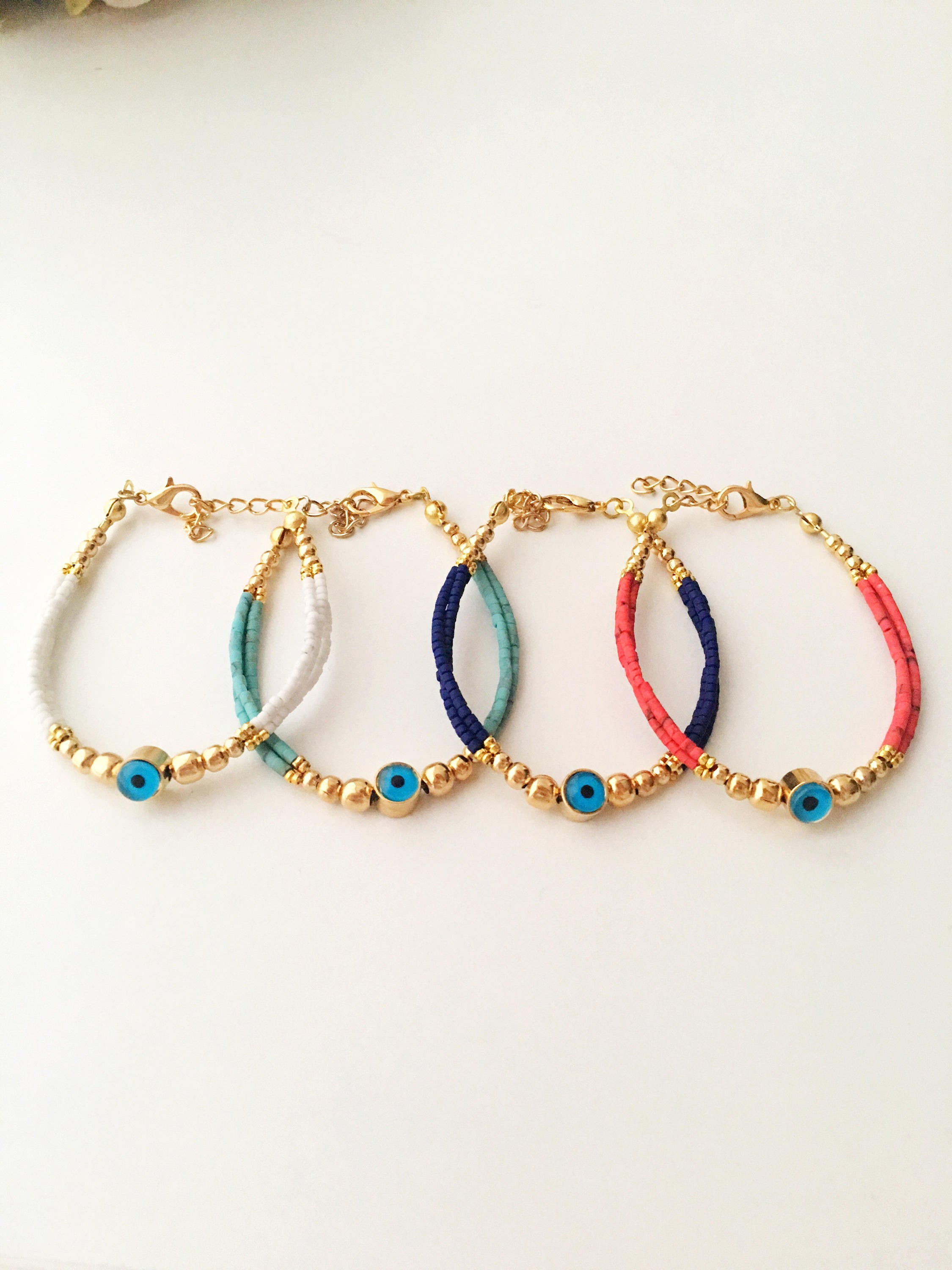 Handmade Greek Evil Eye Bracelet featuring vibrant seed beads and gold accents, available in turquoise, dark blue, red, and white.