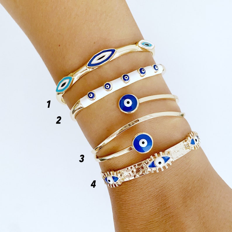 A beautiful Greek Evil Eye Cuff Bracelet featuring a blue evil eye design on a gold adjustable cuff, symbolizing protection and good luck.