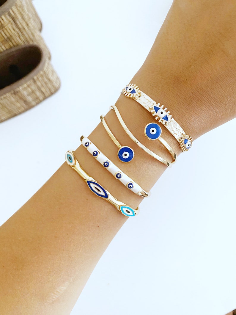 A beautiful Greek Evil Eye Cuff Bracelet featuring a blue evil eye design on a gold adjustable cuff, symbolizing protection and good luck.