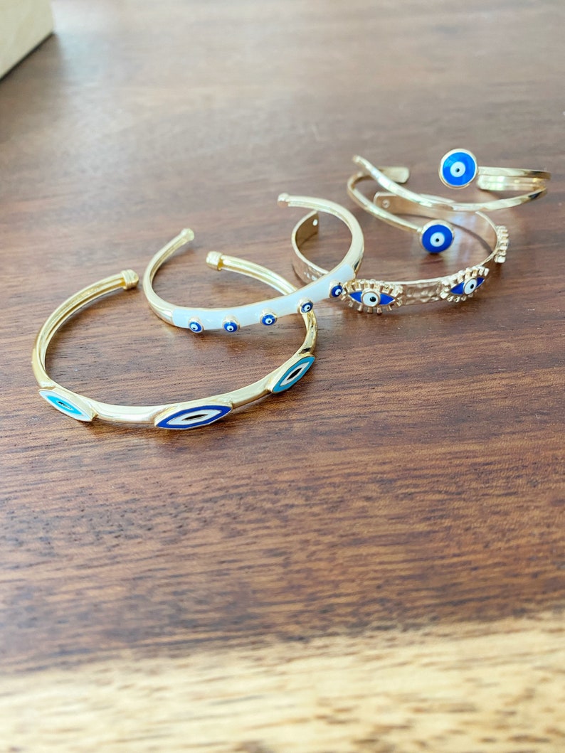 A beautiful Greek Evil Eye Cuff Bracelet featuring a blue evil eye design on a gold adjustable cuff, symbolizing protection and good luck.