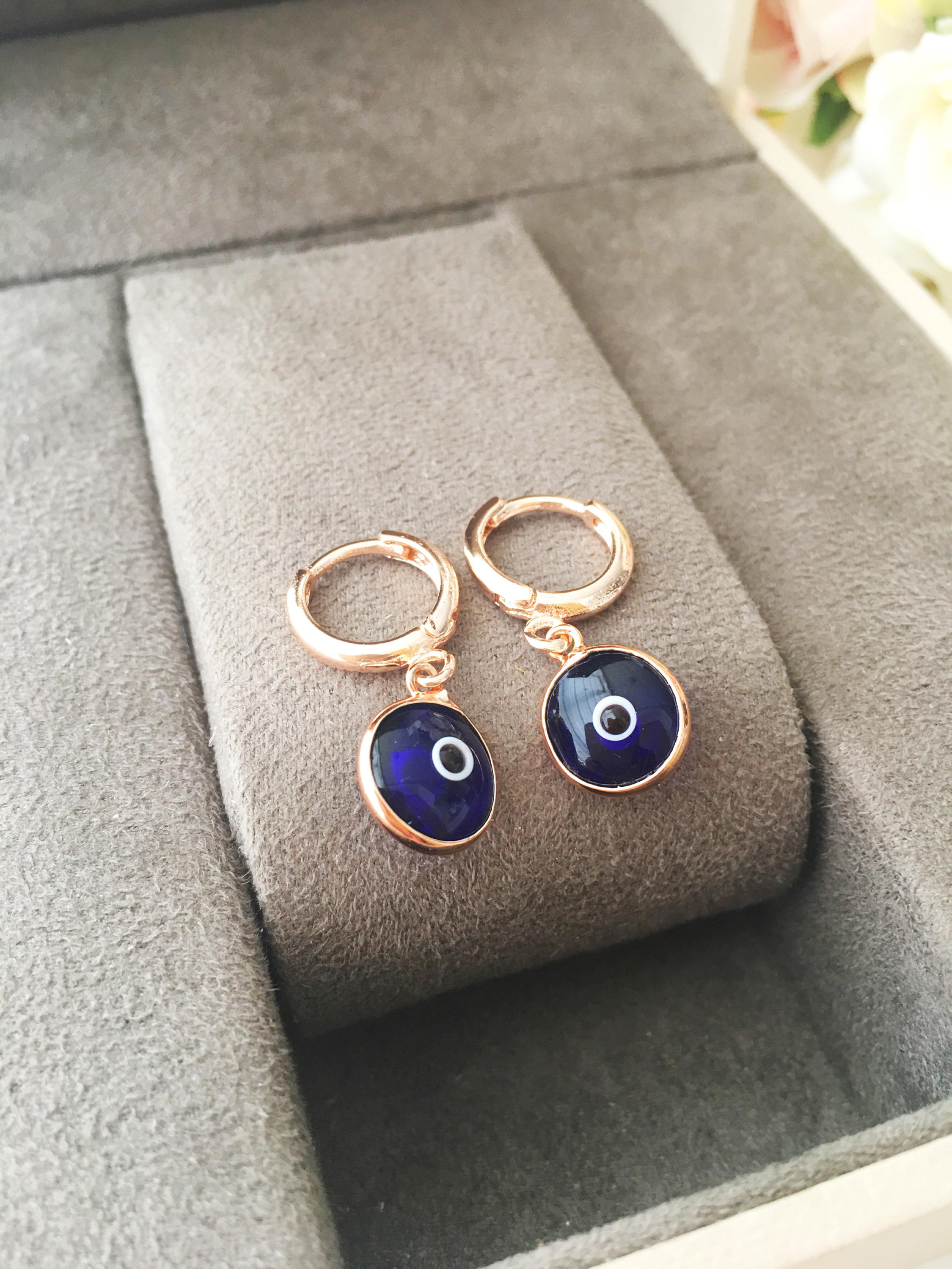 A pair of handmade Greek Evil Eye Hoop Earrings featuring blue and turquoise evil eye charms on gold hoops.