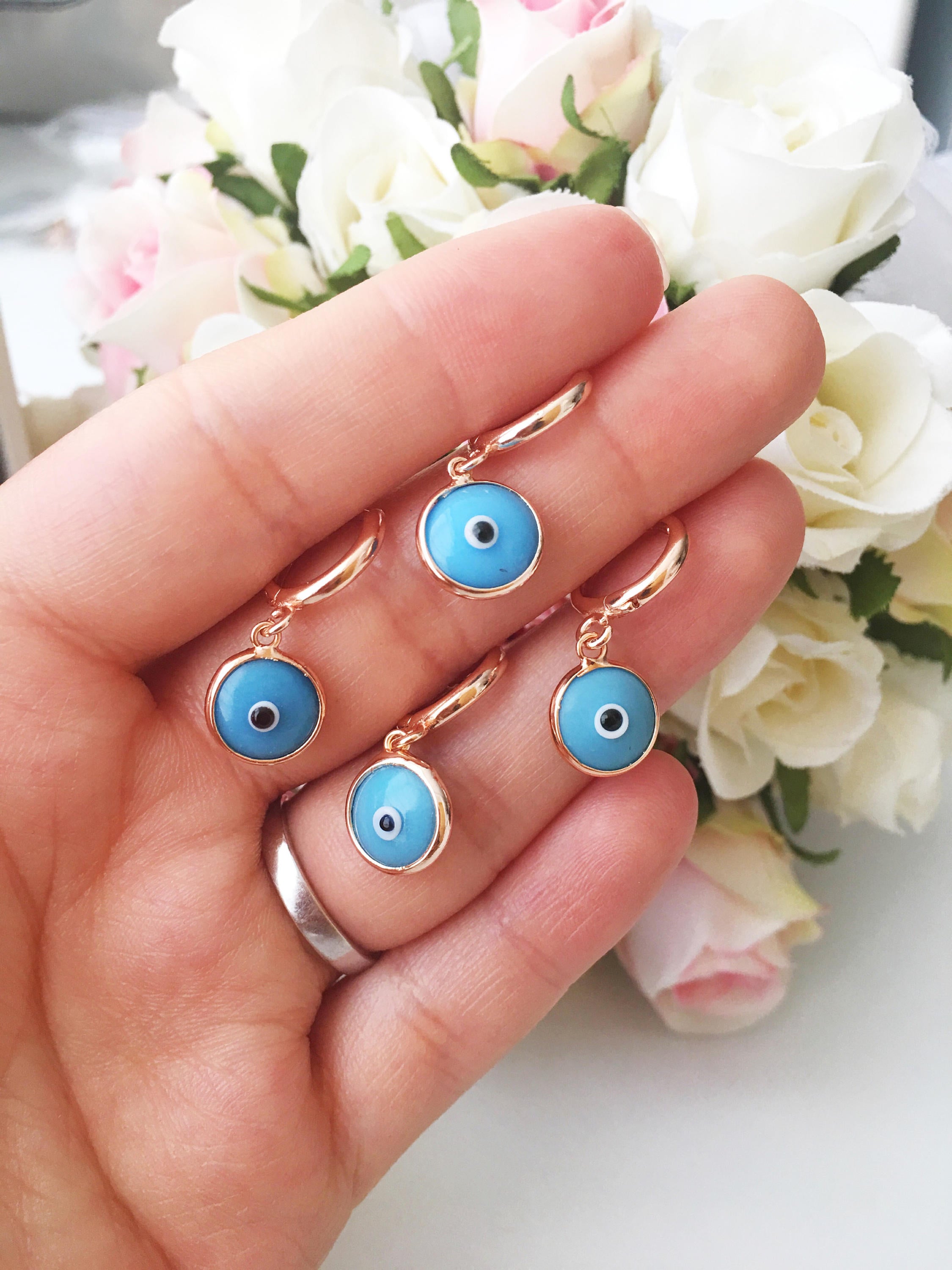 A pair of handmade Greek Evil Eye Hoop Earrings featuring blue and turquoise evil eye charms on gold hoops.