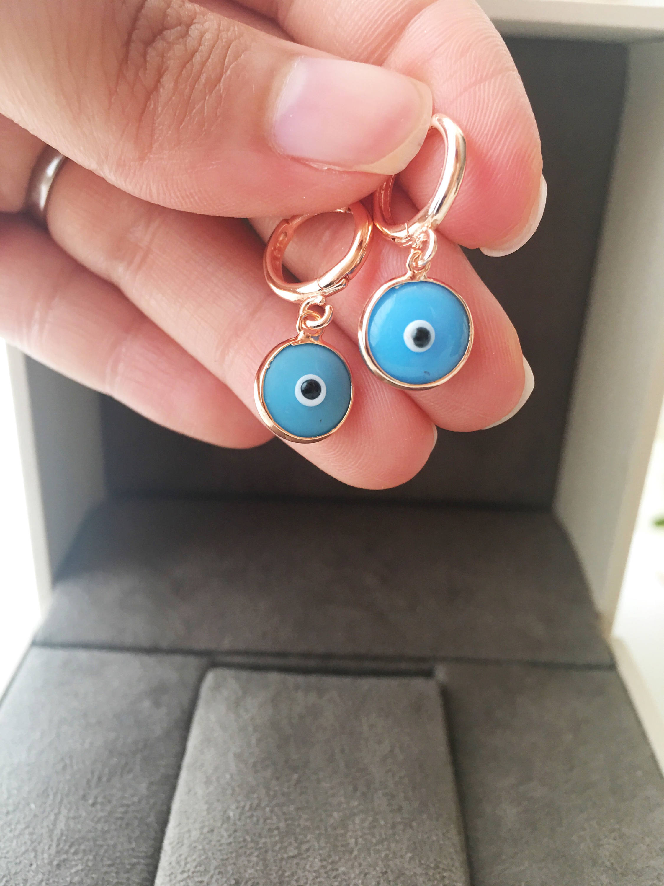 A pair of handmade Greek Evil Eye Hoop Earrings featuring blue and turquoise evil eye charms on gold hoops.