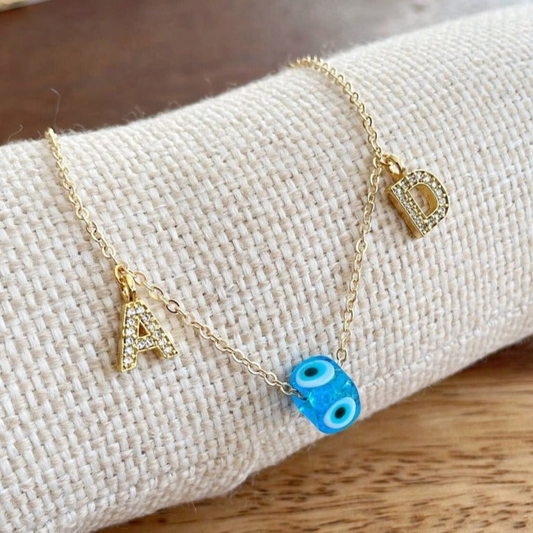 A beautiful Greek Evil Eye Necklace featuring a blue glass bead and 14K gold chain with customizable initials.