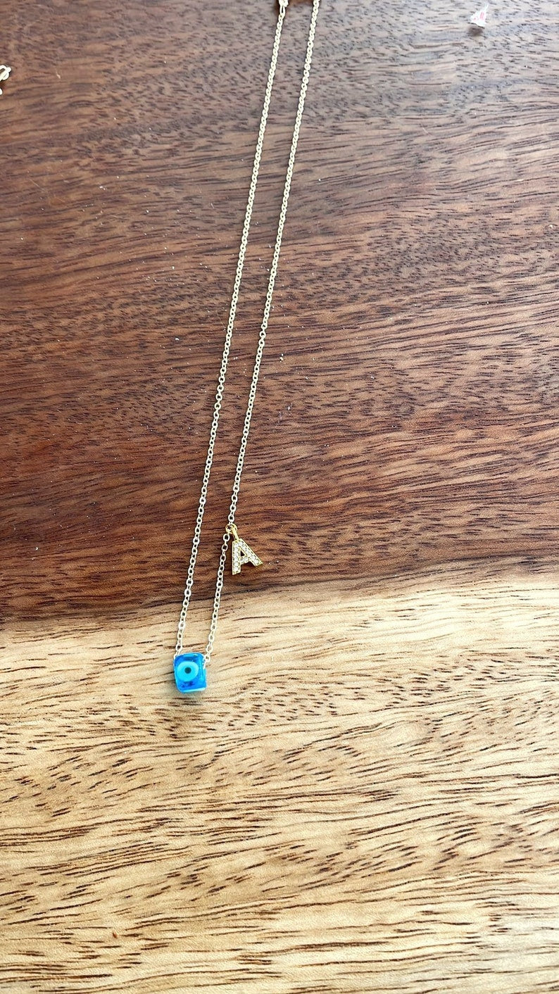 A beautiful Greek Evil Eye Necklace featuring a blue glass bead and 14K gold chain with customizable initials.