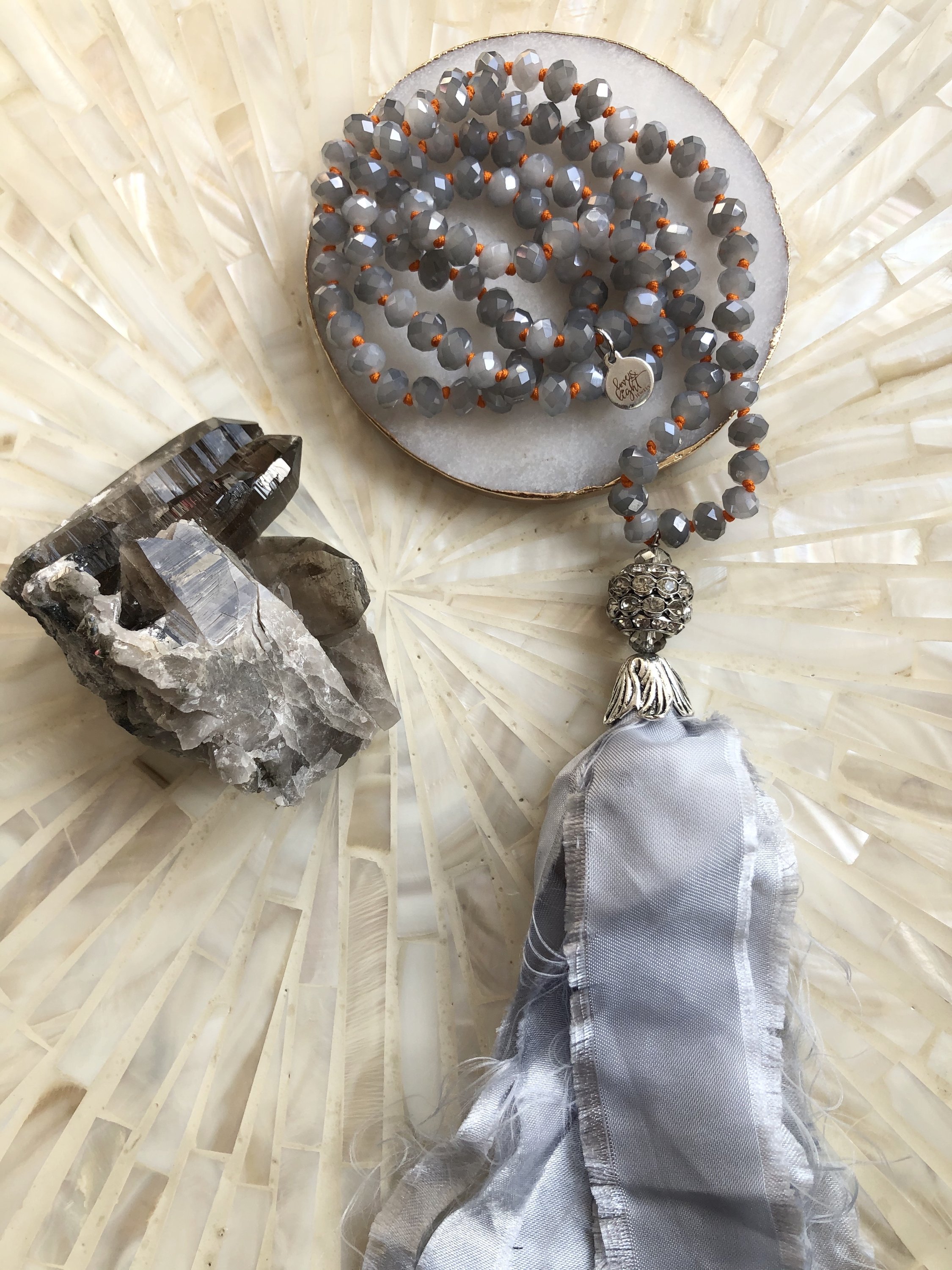 A stylish Grey Sari Tassel Necklace featuring grey crystal beads, a satin tassel, and a sparkling rhinestone encrusted pendant.