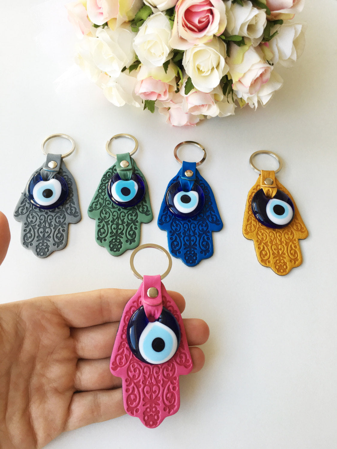 A stylish Hamsa hand evil eye keychain made of faux leather with a blue glass evil eye bead, available in various colors.