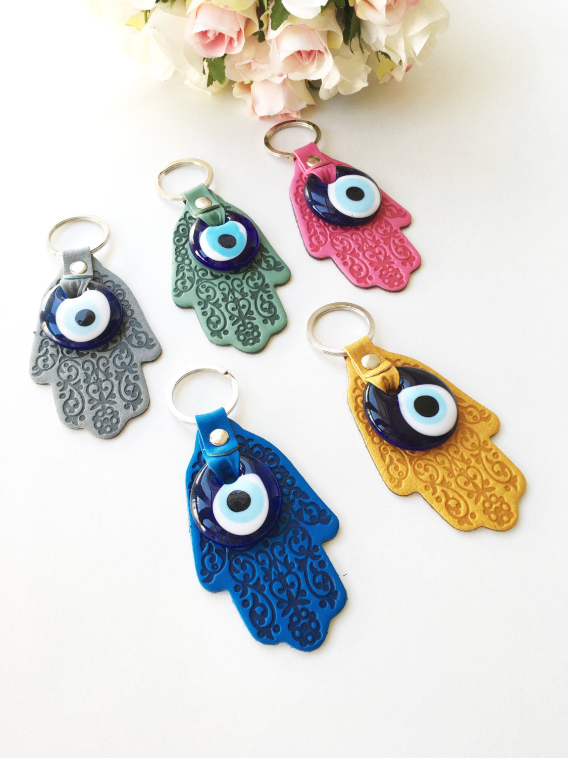 A stylish Hamsa hand evil eye keychain made of faux leather with a blue glass evil eye bead, available in various colors.