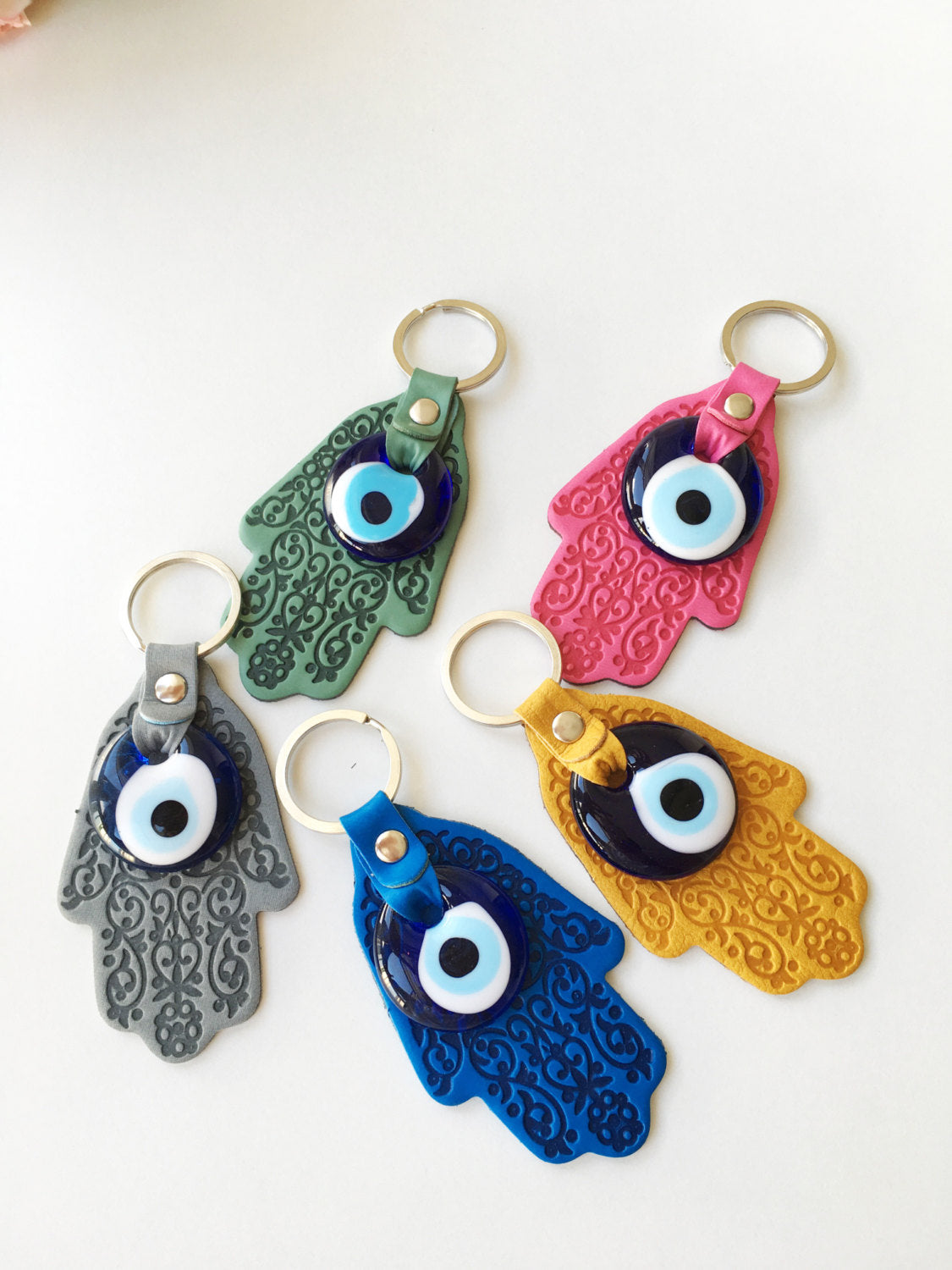 A stylish Hamsa hand evil eye keychain made of faux leather with a blue glass evil eye bead, available in various colors.