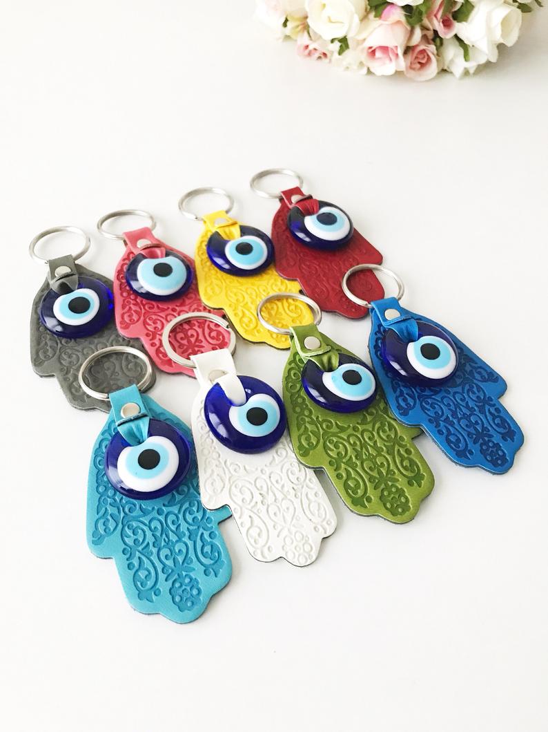 A stylish Hamsa hand evil eye keychain made of faux leather with a blue glass evil eye bead, available in various colors.