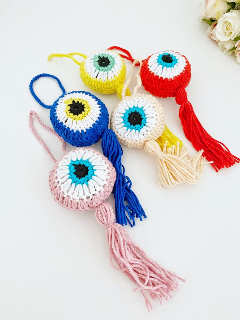 A beautifully crafted Handmade Evil Eye wall hanging featuring a vibrant blue eye symbol, intricately knitted, perfect for home decor or as a car charm.