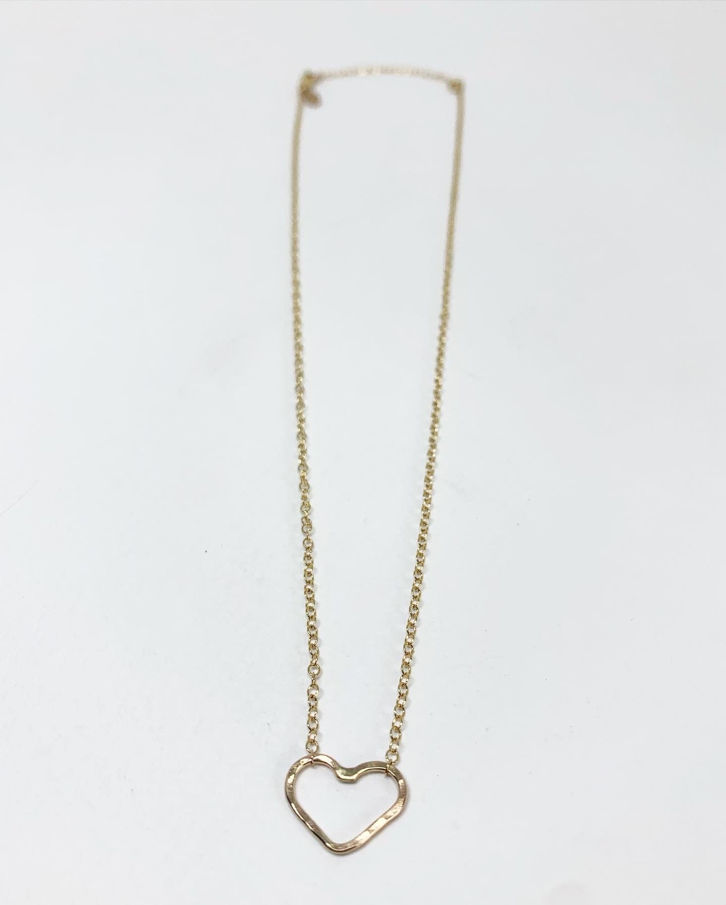 A delicate heart charm necklace featuring a rustic hammered heart pendant on an adjustable cable chain, symbolizing love and joy.