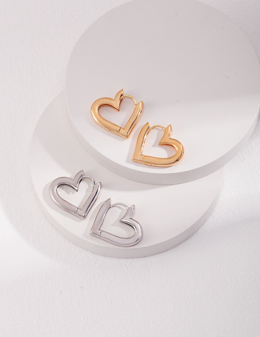 A pair of elegant heart shape hoop earrings made from sterling silver with a gold vermeil finish, showcasing their unique design and craftsmanship.