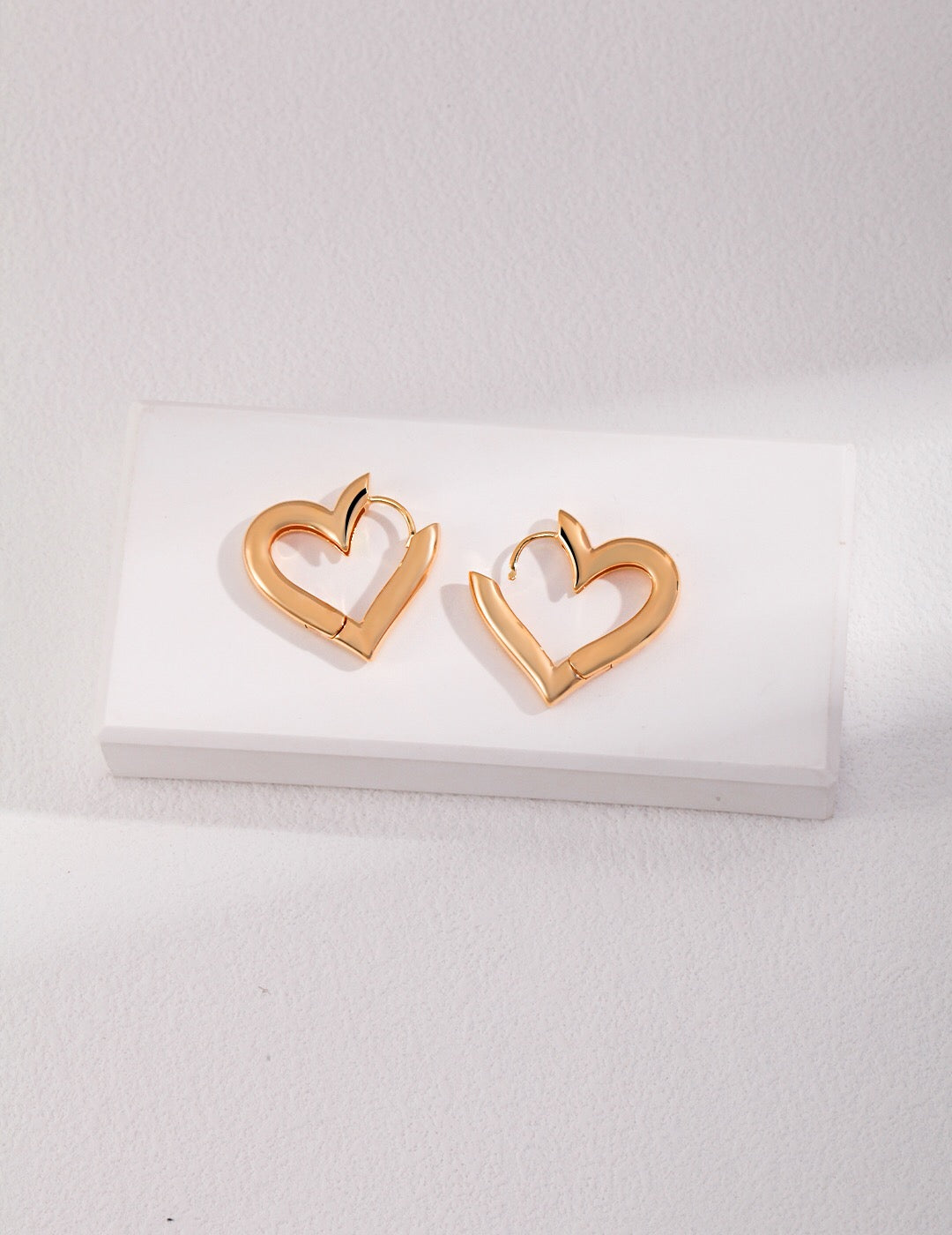 A pair of elegant heart shape hoop earrings made from sterling silver with a gold vermeil finish, showcasing their unique design and craftsmanship.