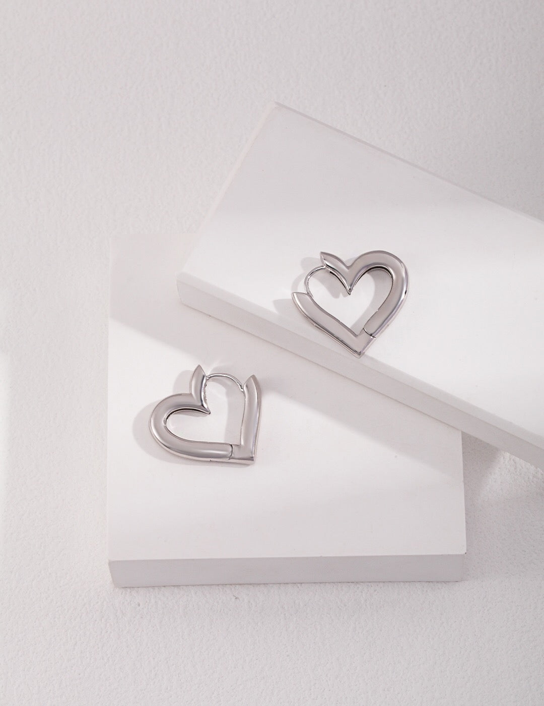 A pair of elegant heart shape hoop earrings made from sterling silver with a gold vermeil finish, showcasing their unique design and craftsmanship.