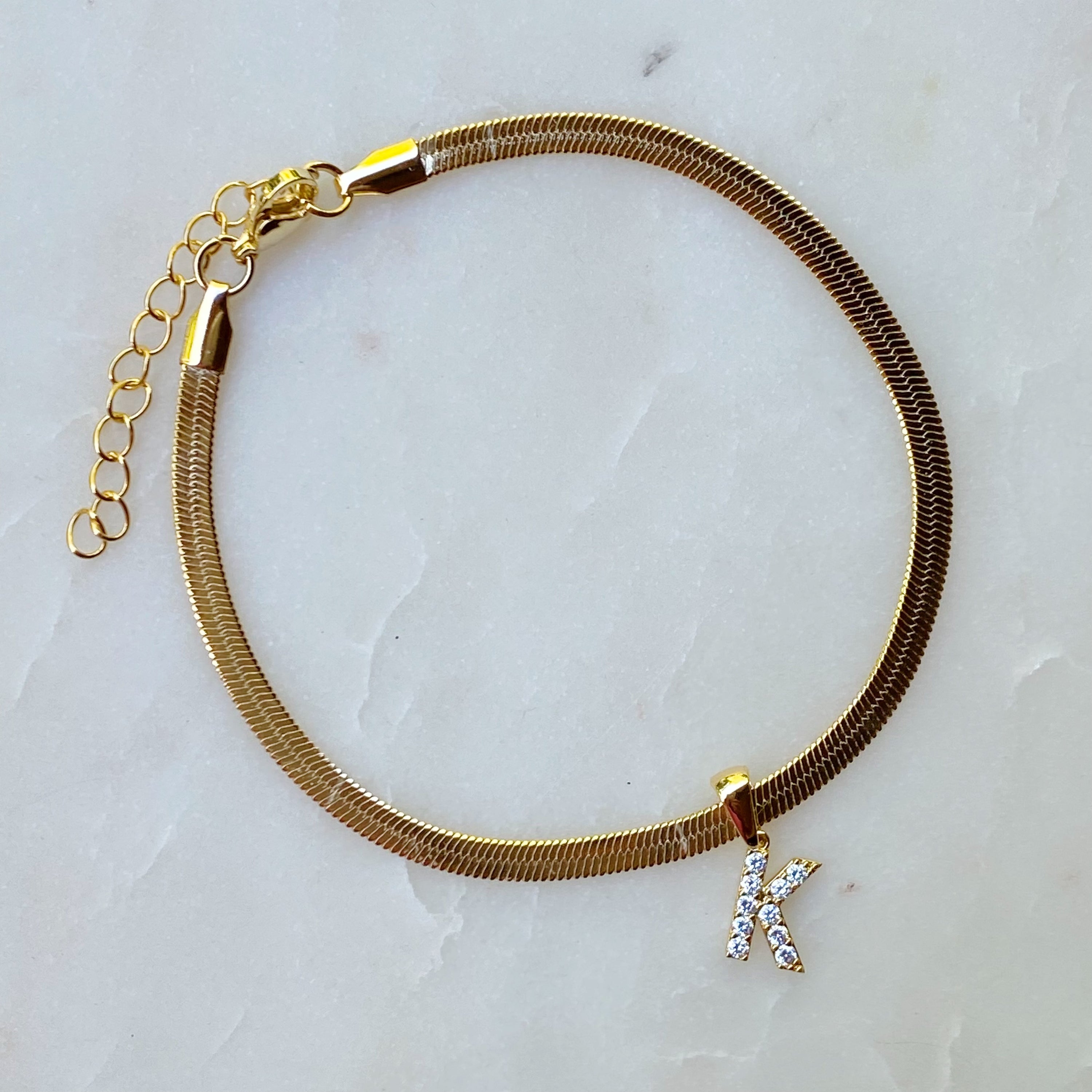 Elegant Herringbone Chain Initial Anklet with shiny initial charm, showcasing its gold plating and adjustable length.