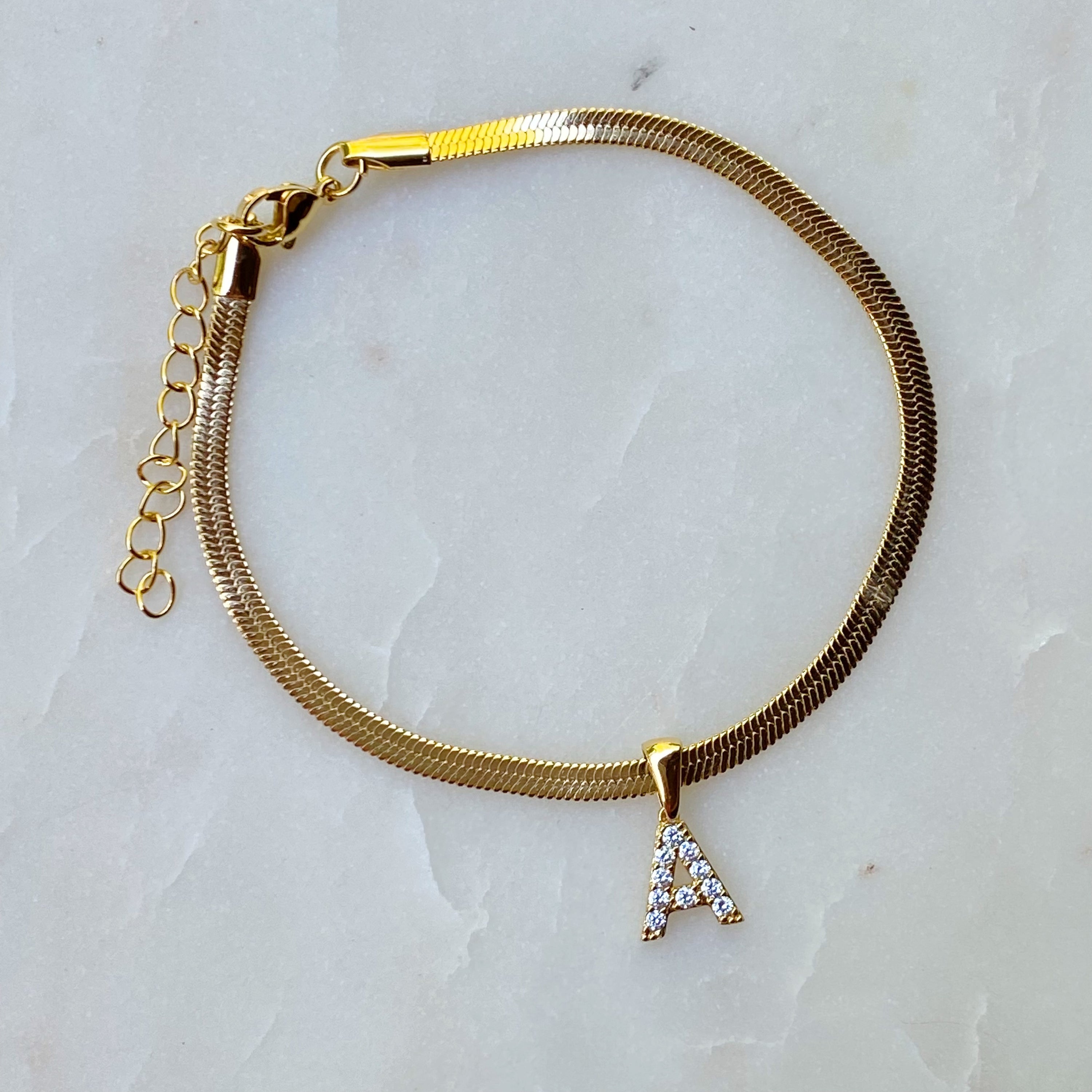 Elegant Herringbone Chain Initial Anklet with shiny initial charm, showcasing its gold plating and adjustable length.