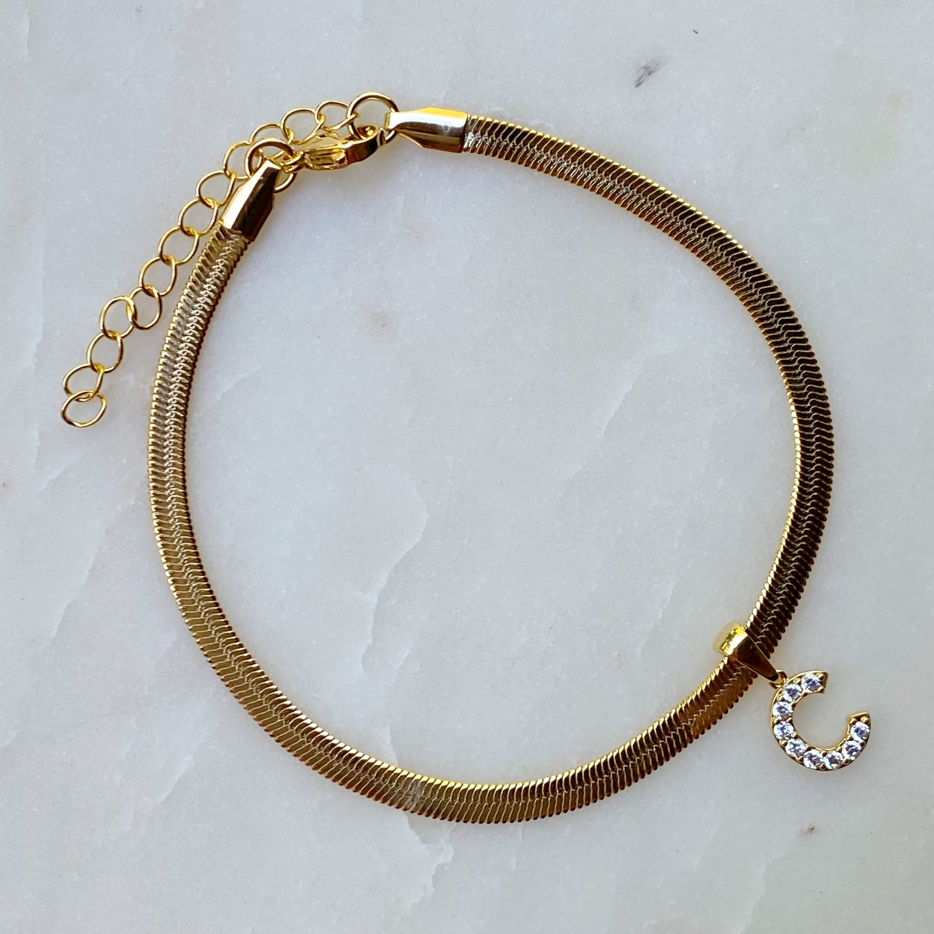 Elegant Herringbone Chain Initial Anklet with shiny initial charm, showcasing its gold plating and adjustable length.