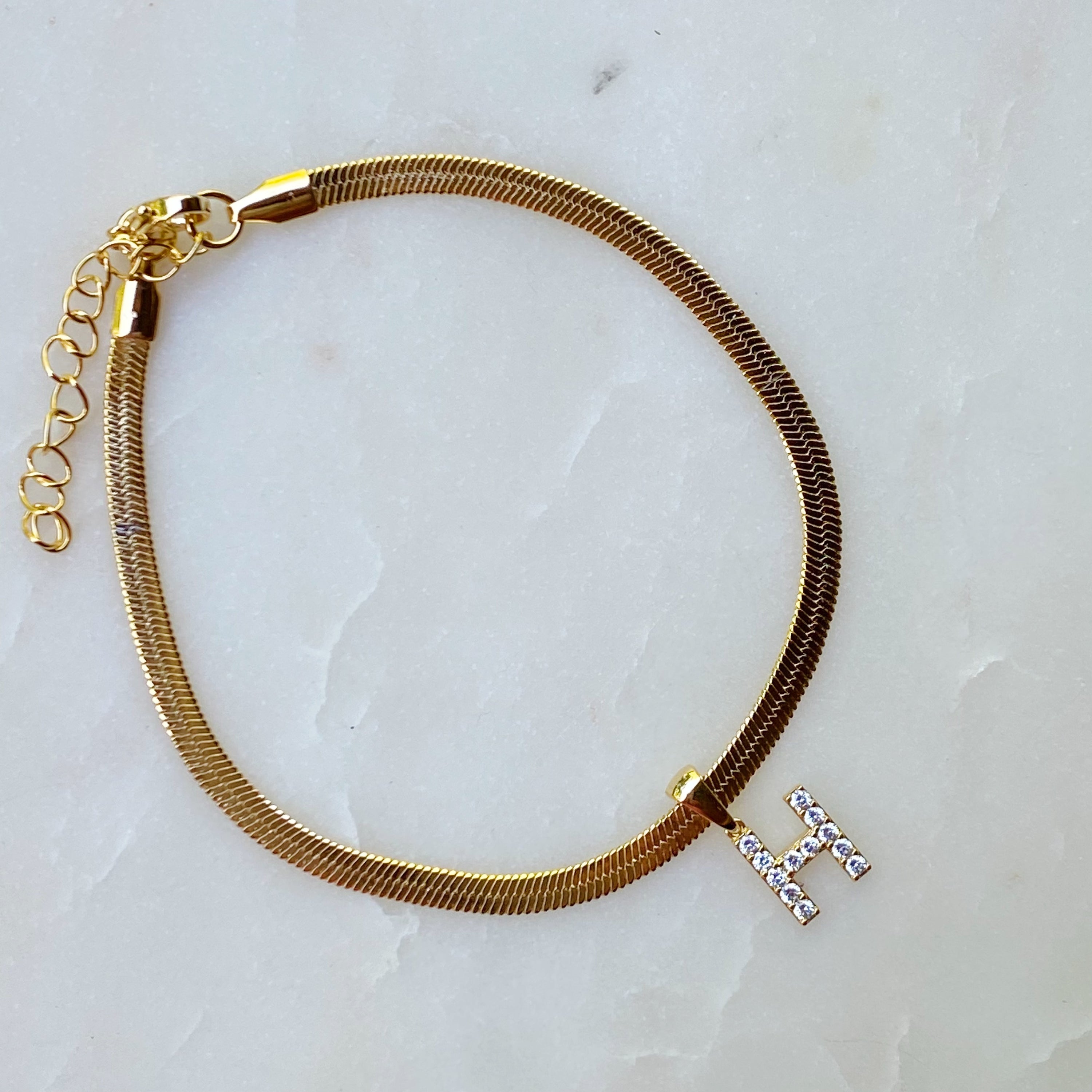 Elegant Herringbone Chain Initial Anklet with shiny initial charm, showcasing its gold plating and adjustable length.