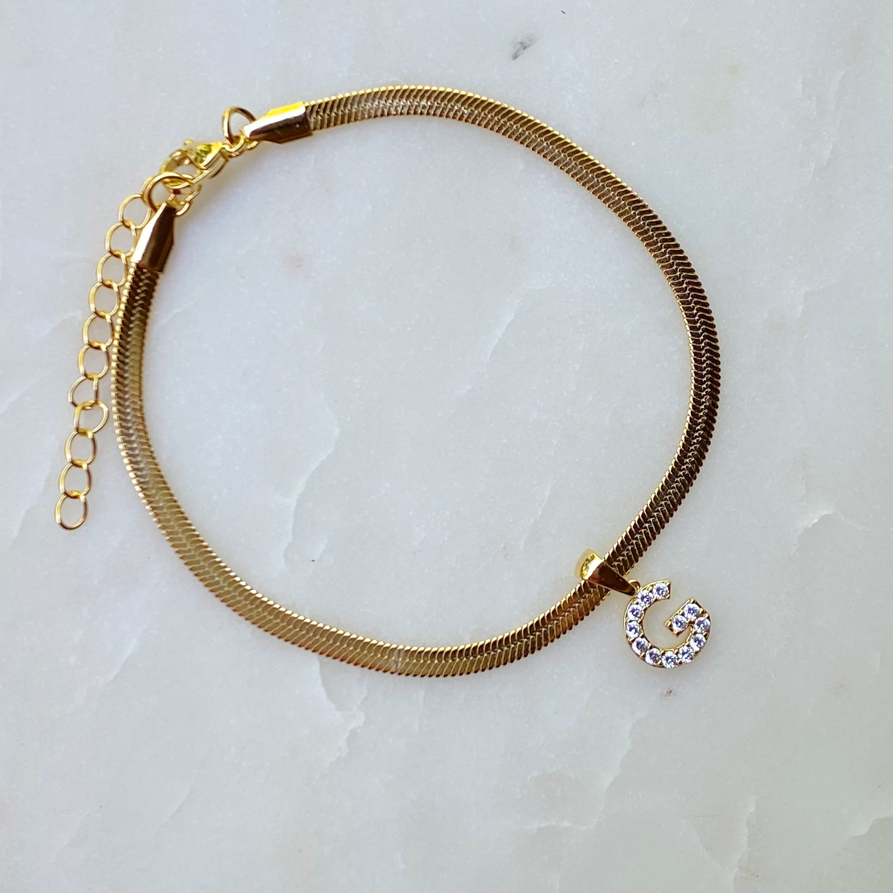 Elegant Herringbone Chain Initial Anklet with shiny initial charm, showcasing its gold plating and adjustable length.