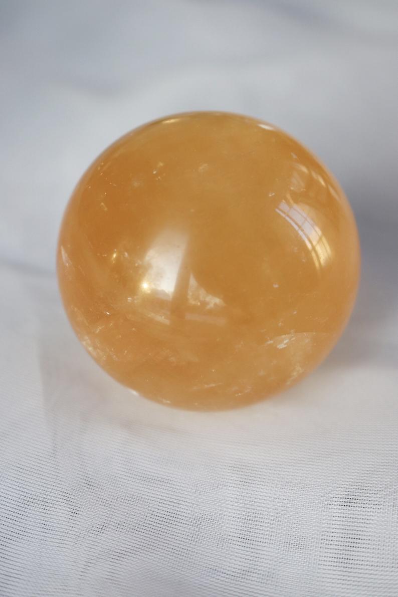 A beautifully hand-carved Honey Calcite Sphere with a warm yellow glow, showcasing its unique textures and natural markings.