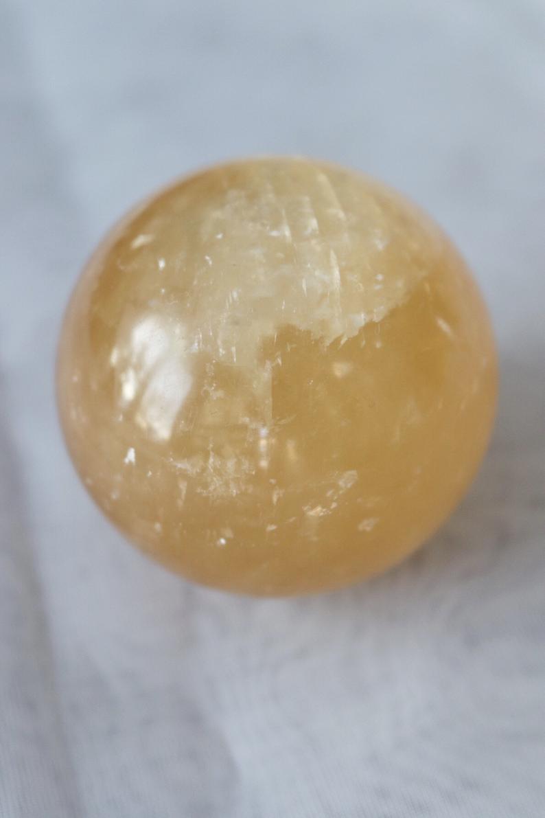 A beautifully hand-carved Honey Calcite Sphere with a warm yellow glow, showcasing its unique textures and natural markings.