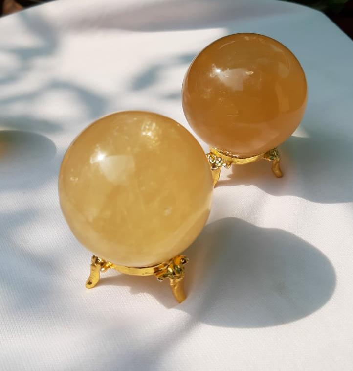 A beautifully hand-carved Honey Calcite Sphere with a warm yellow glow, showcasing its unique textures and natural markings.