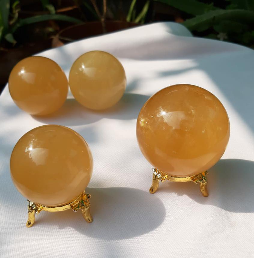 A beautifully hand-carved Honey Calcite Sphere with a warm yellow glow, showcasing its unique textures and natural markings.