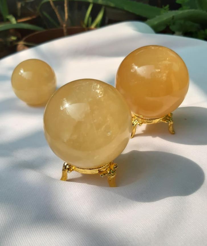 A beautifully hand-carved Honey Calcite Sphere with a warm yellow glow, showcasing its unique textures and natural markings.