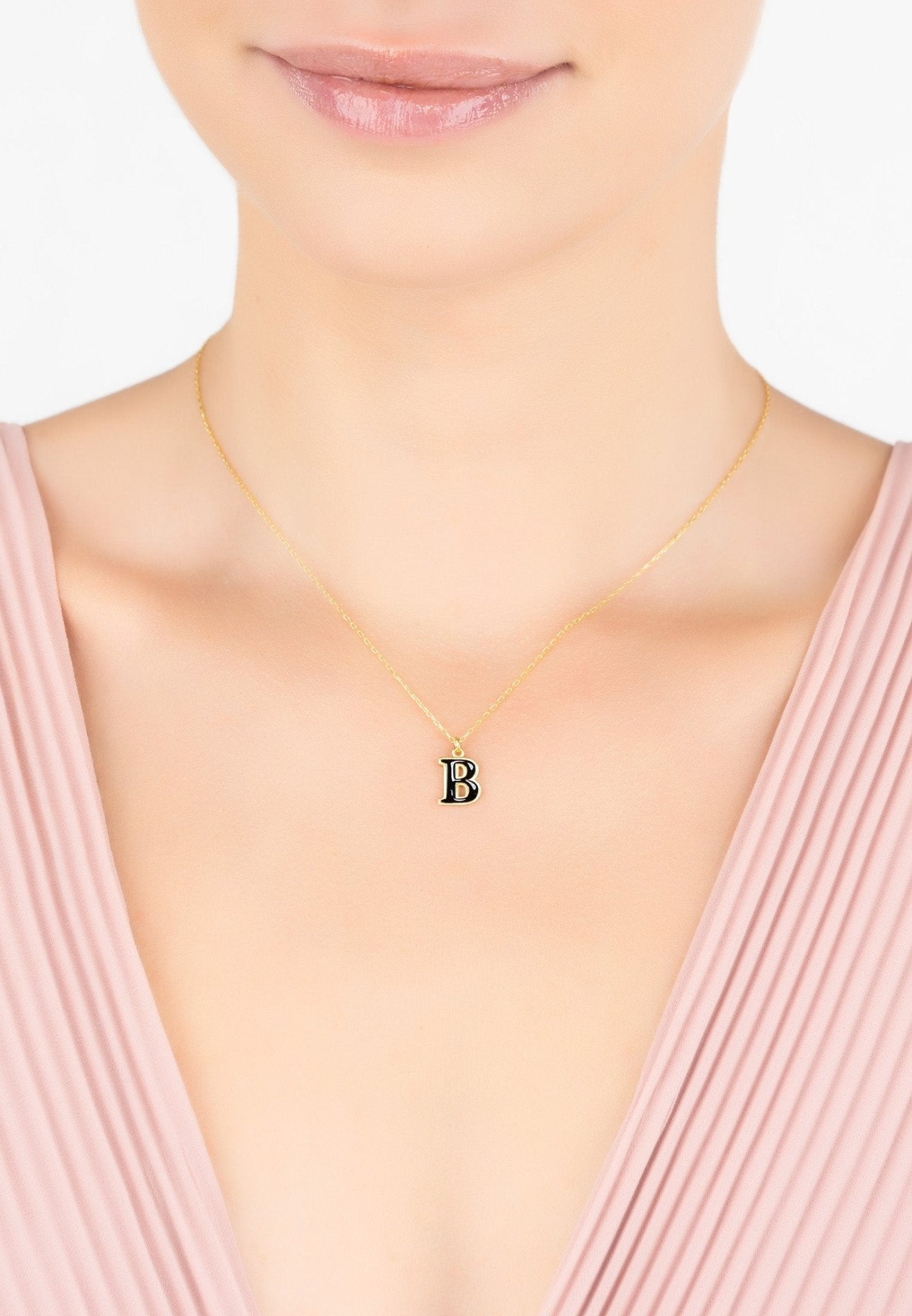 A delicate gold necklace featuring an initial pendant with black enamel inlay, elegantly displayed in a jewelry box.