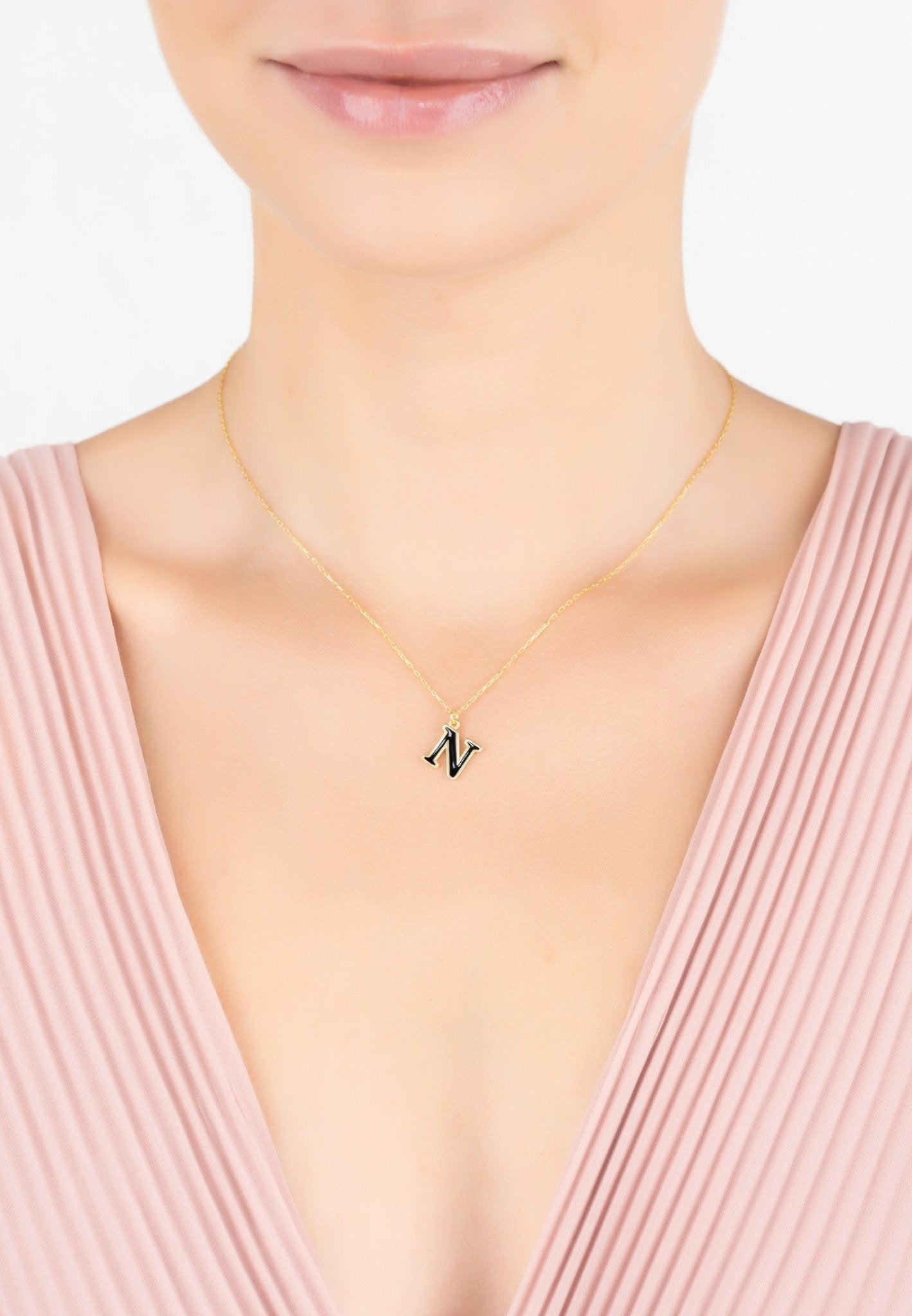 A delicate gold initial enamel necklace featuring a black enamel inlay, elegantly displayed in a jewelry box.