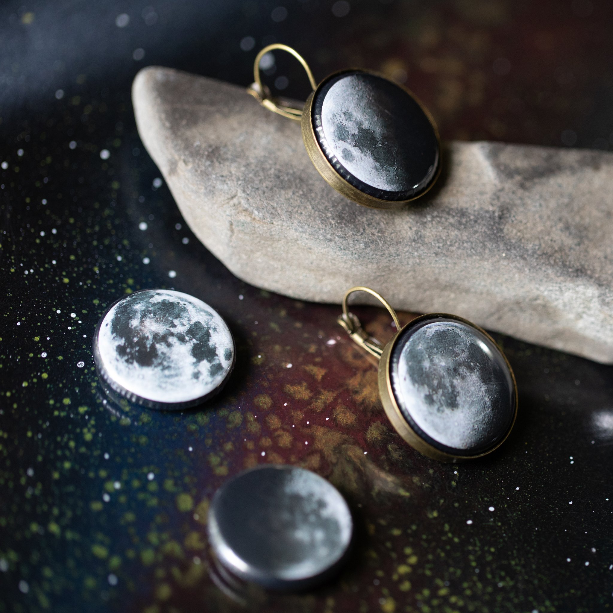 A pair of interchangeable earrings featuring five moon phases, available in silver and bronze tones, showcasing their unique magnetic design.