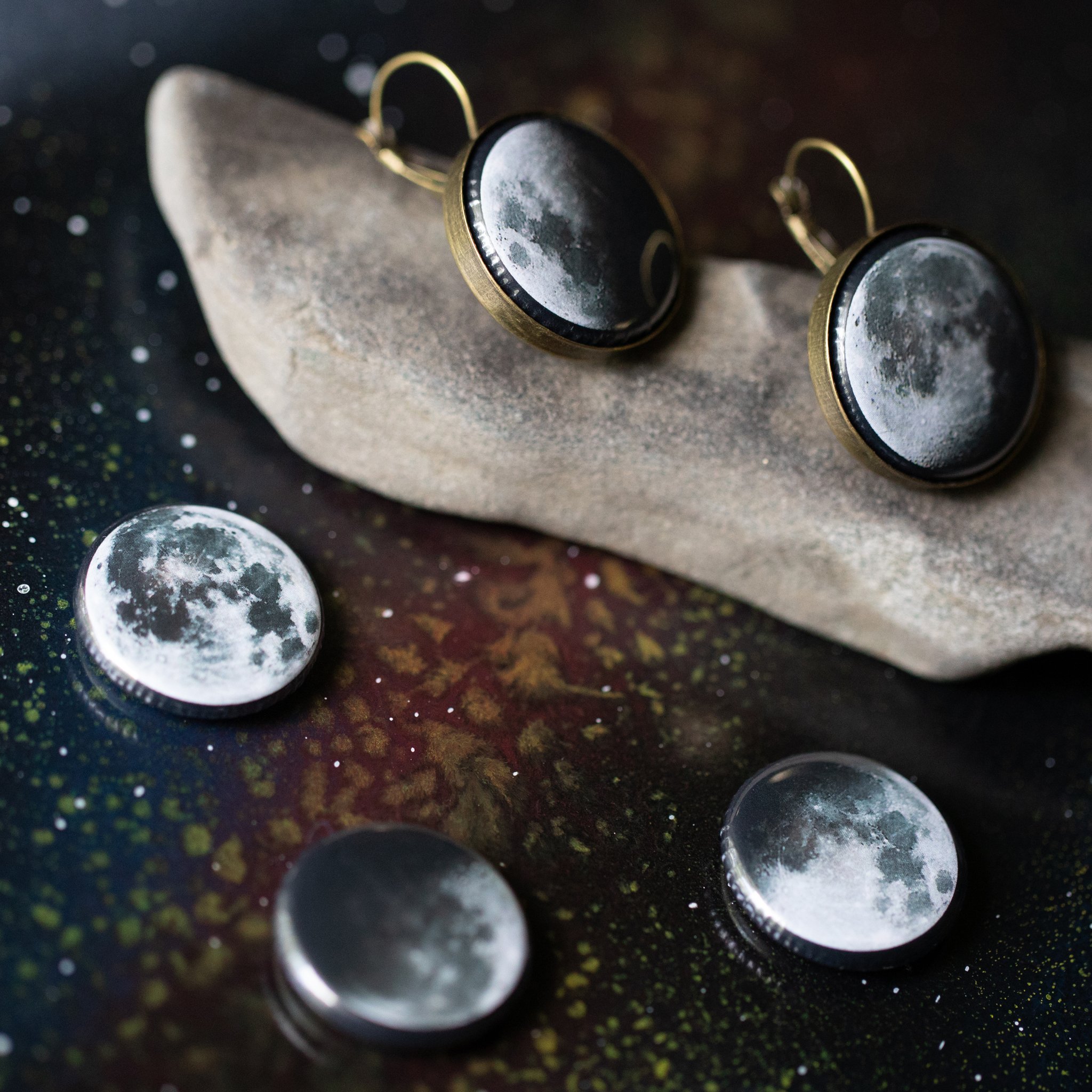 A pair of interchangeable earrings featuring five moon phases, available in silver and bronze tones, showcasing their unique magnetic design.