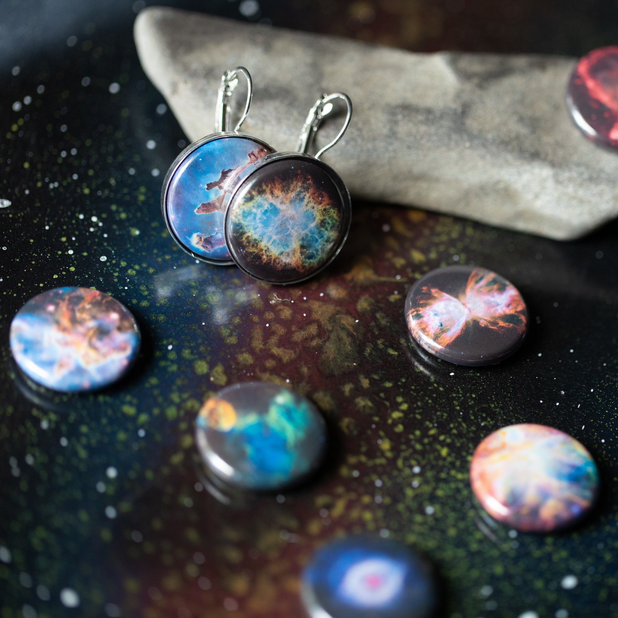 A pair of Interchangeable Nebula Earrings showcasing vibrant cosmic designs, available in silver and bronze tones, with a strong magnetic hold.