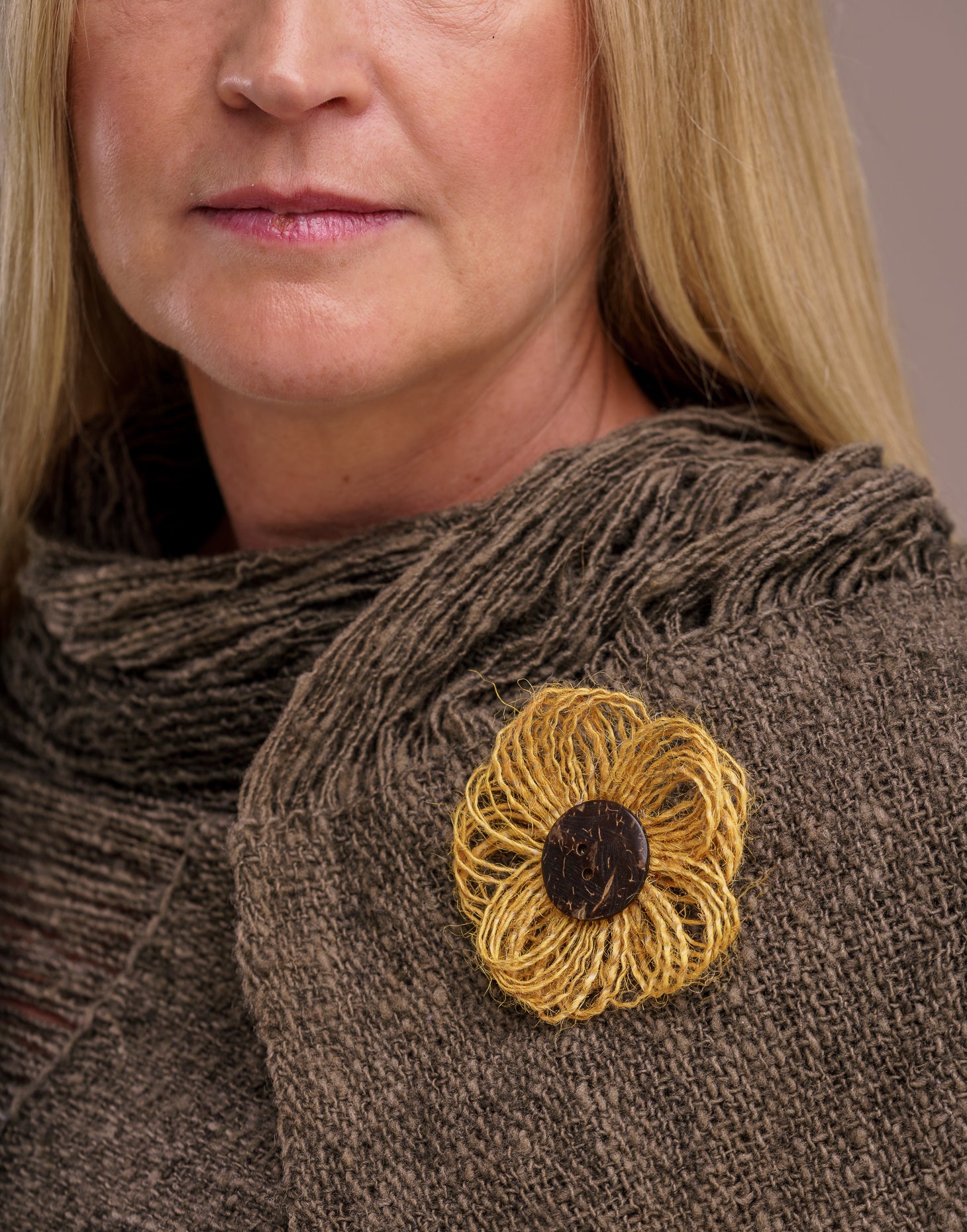 A delicate jute flower brooch featuring a coconut button at the center, showcasing natural fibers and a charming design.