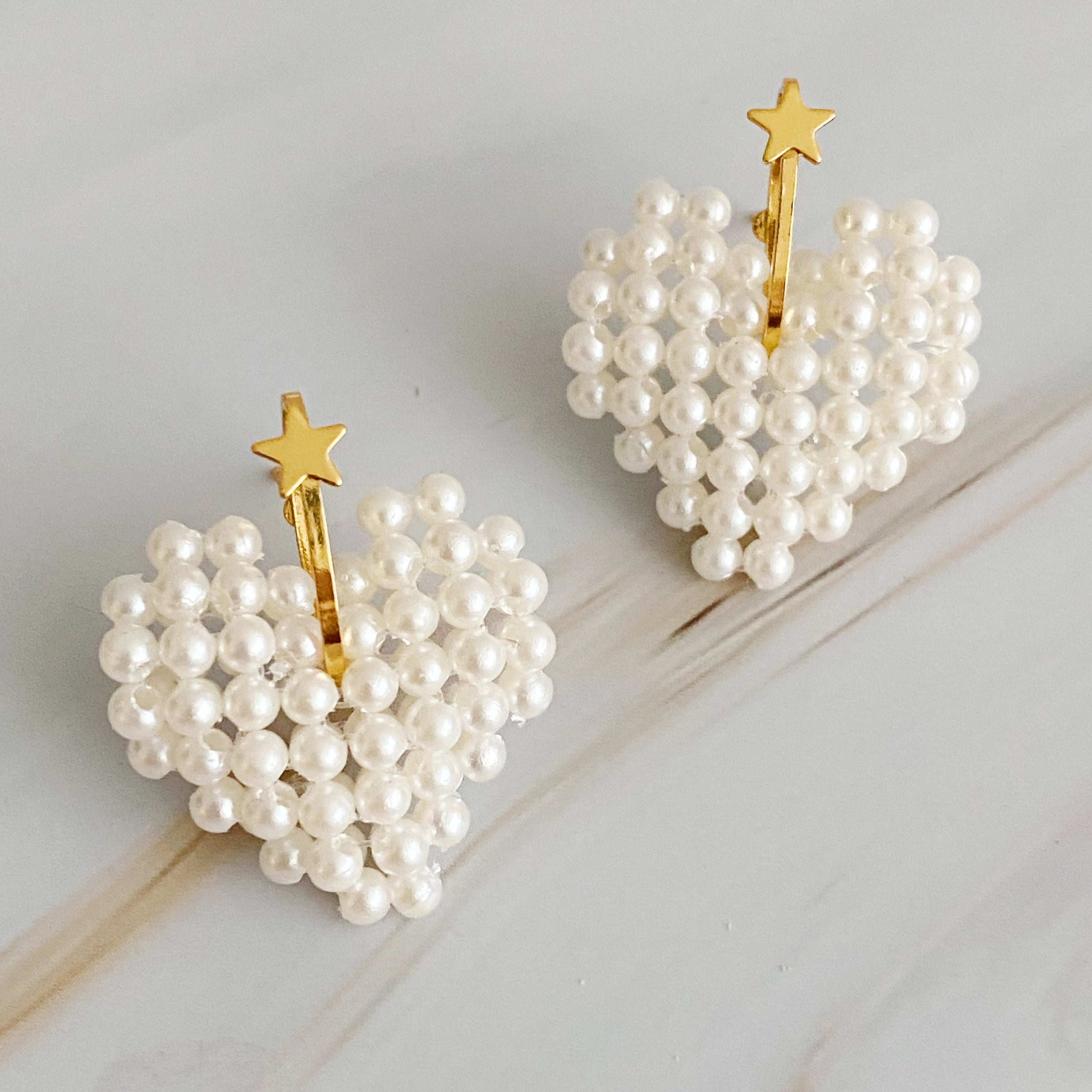 A pair of stylish Knitted Pearl Heart Earrings featuring a knitted pearl heart design with a golden star accent, perfect for any occasion.