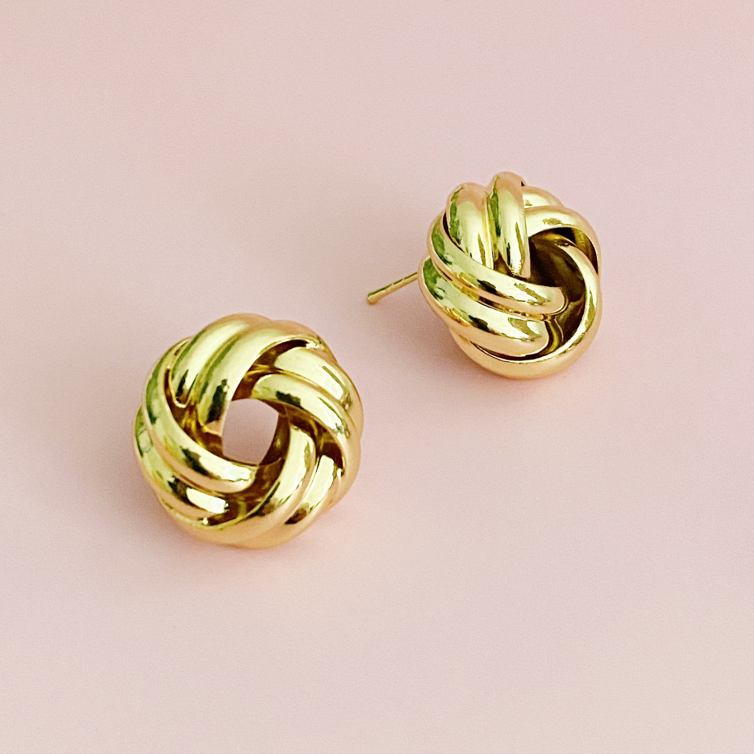 A pair of elegant knotted design stud earrings in polished gold and silver finishes, showcasing their sophisticated craftsmanship.