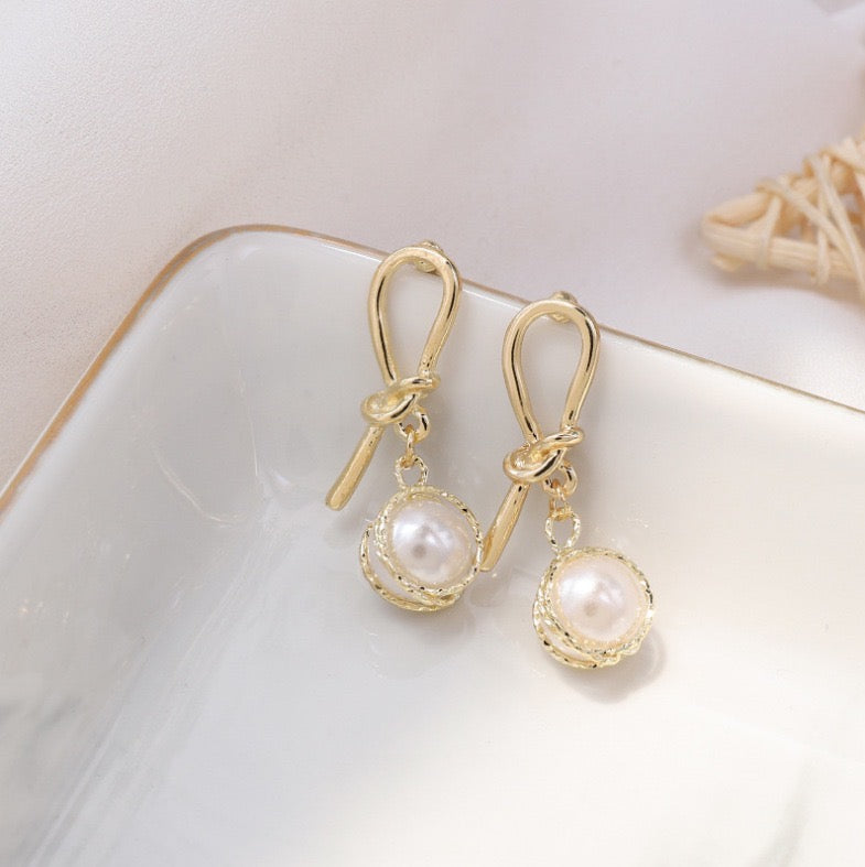 Elegant knotted gold wired earrings featuring a single artificial pearl, perfect for stylish occasions.