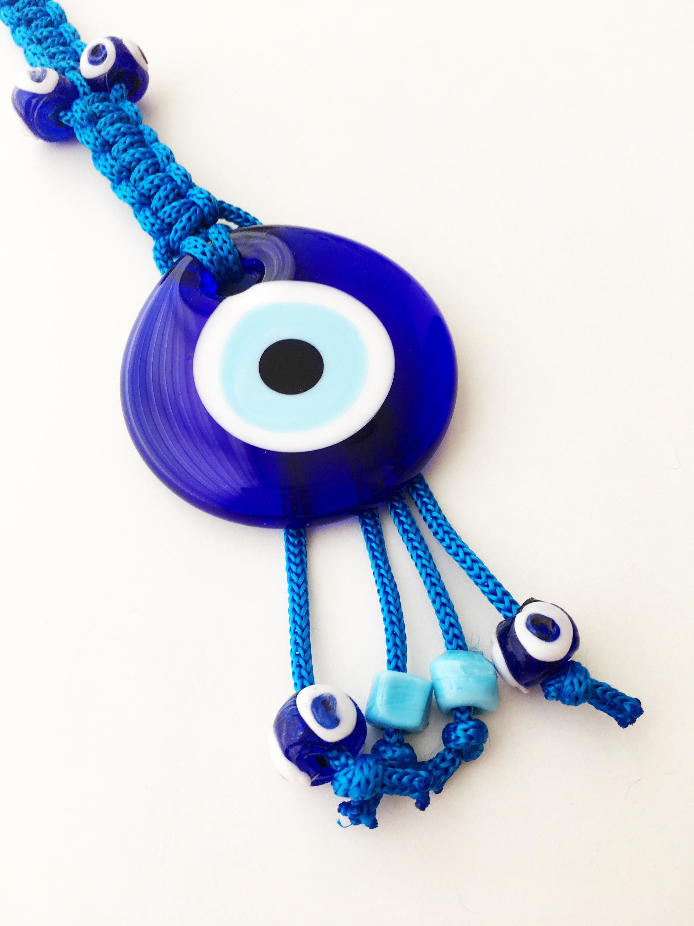 A large blue evil eye wall hanging featuring a central big evil eye bead surrounded by smaller evil eye beads, showcasing intricate macrame design.