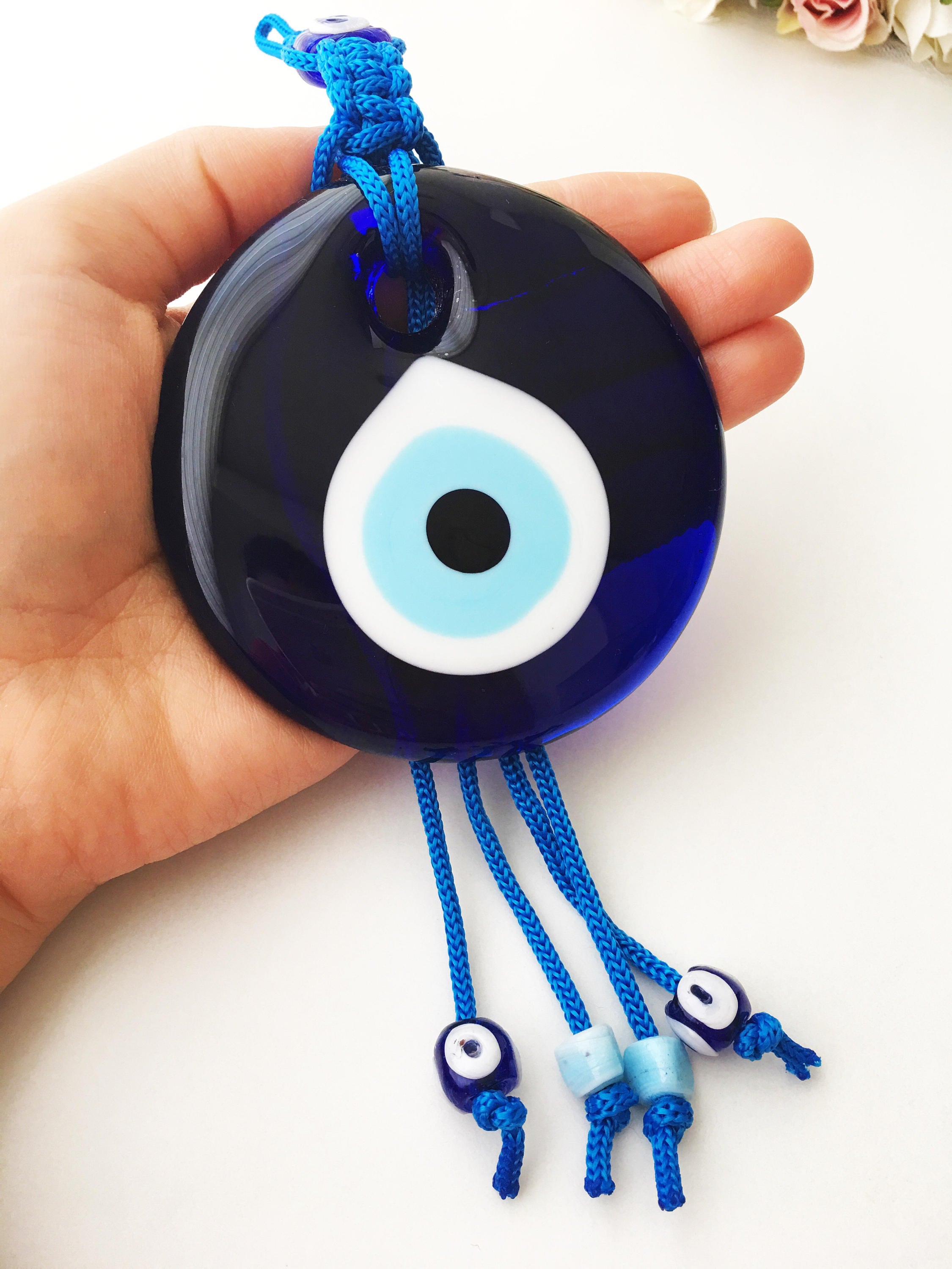 A large blue evil eye wall hanging featuring a central big evil eye bead surrounded by smaller evil eye beads, showcasing intricate macrame design.